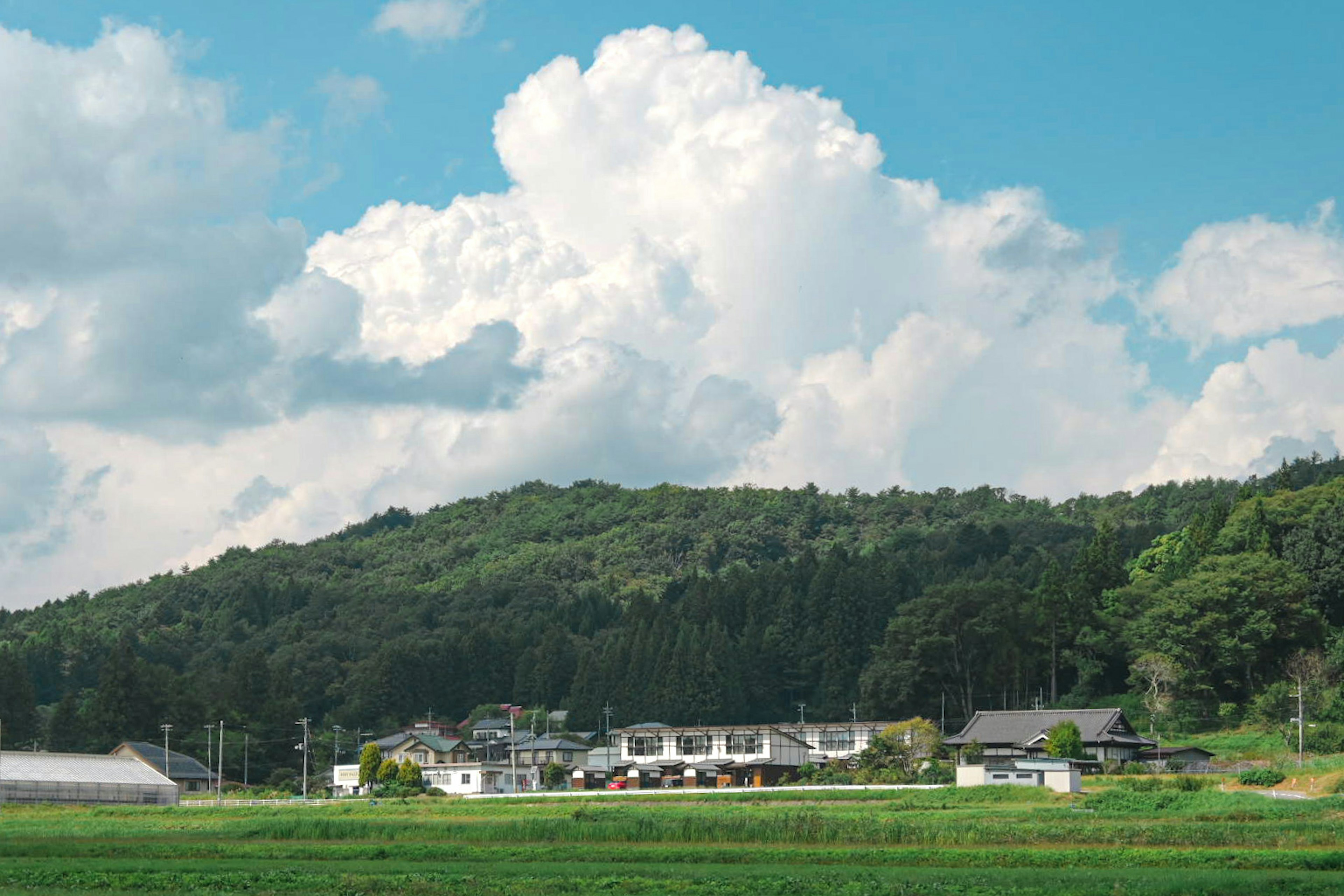 Paisaje rural con casas bajo un cielo azul y nubes blancas