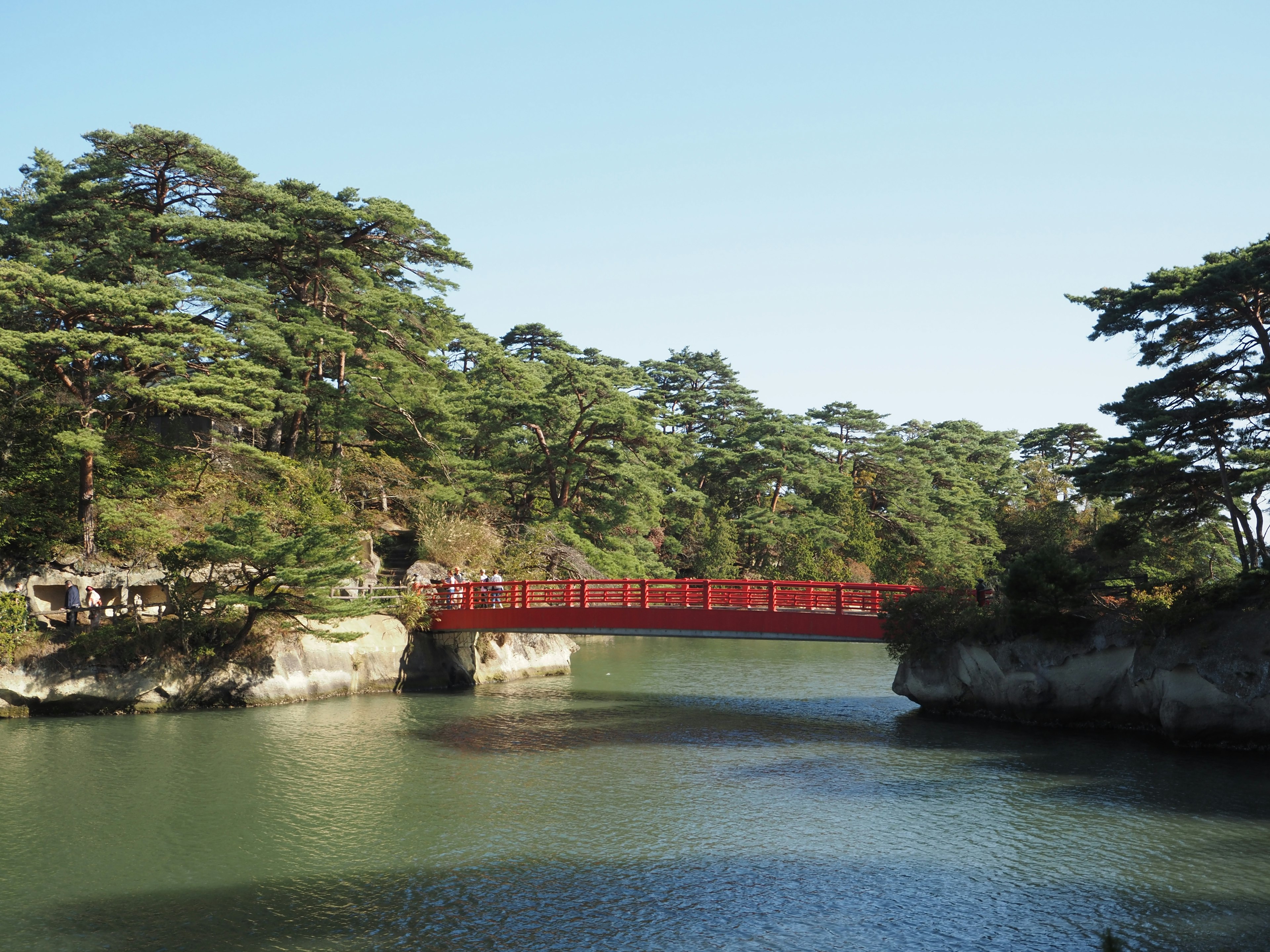 Vue pittoresque avec un pont rouge et des pins verts au bord d'une eau calme