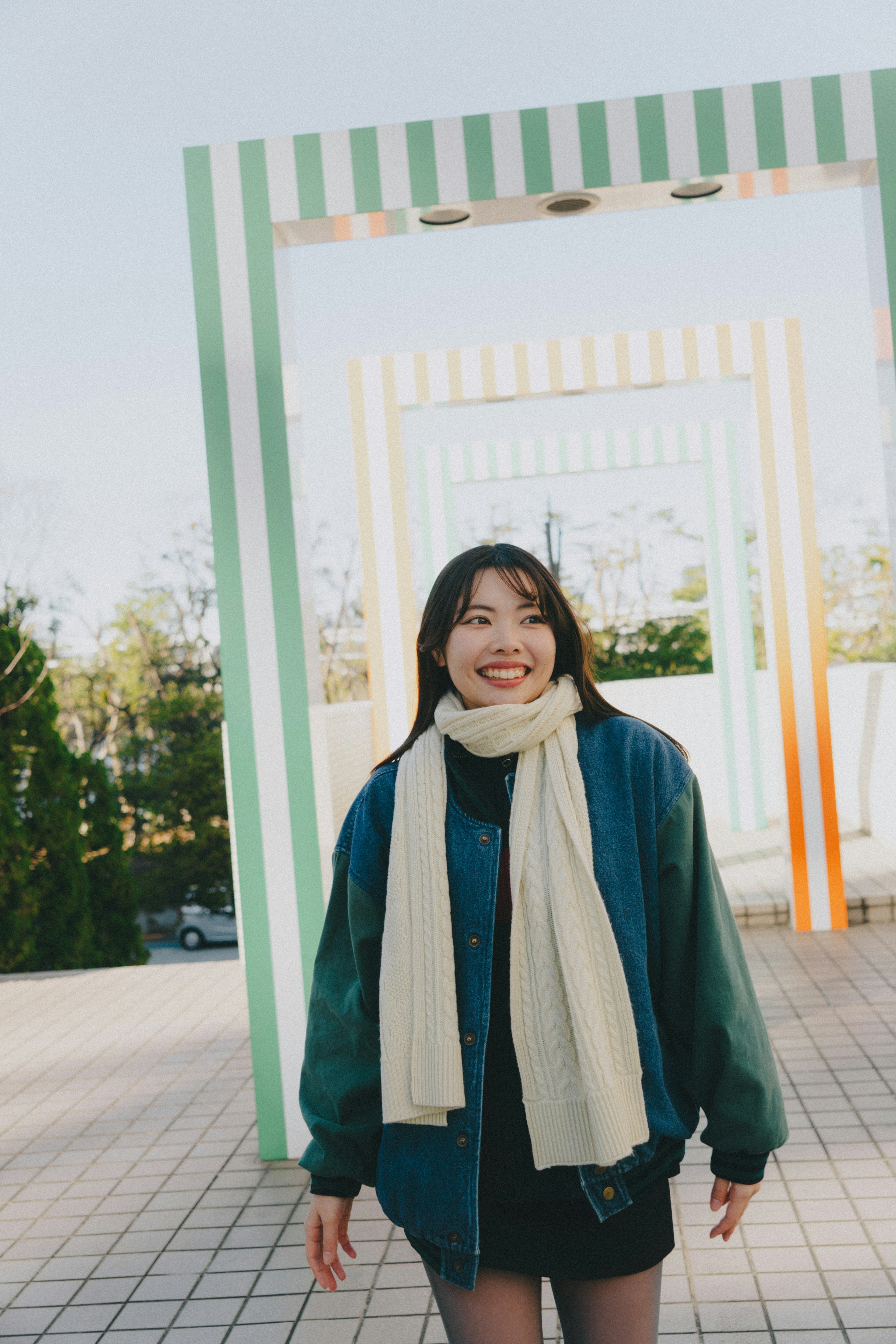 Una mujer sonriente que lleva una chaqueta azul y una bufanda blanca en un entorno exterior brillante