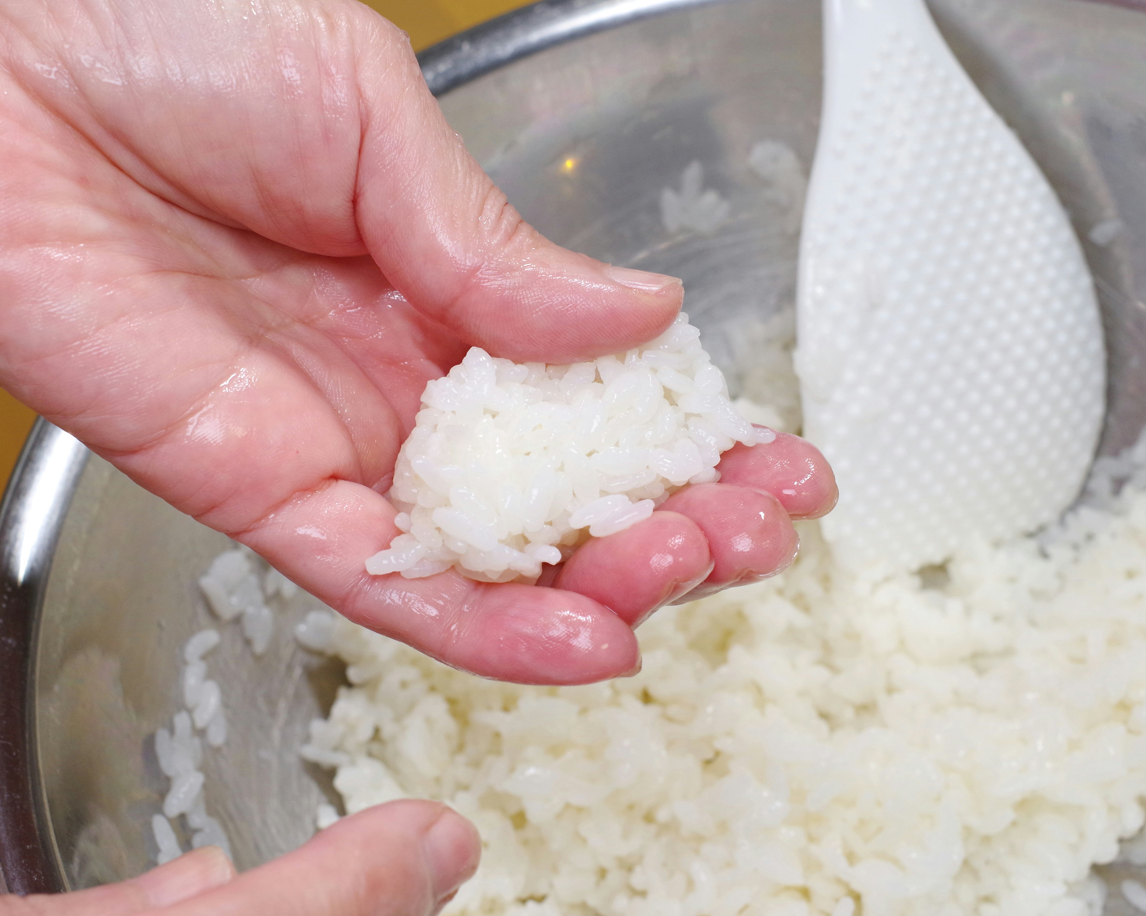 A hand holding a small ball of rice above a bowl of rice