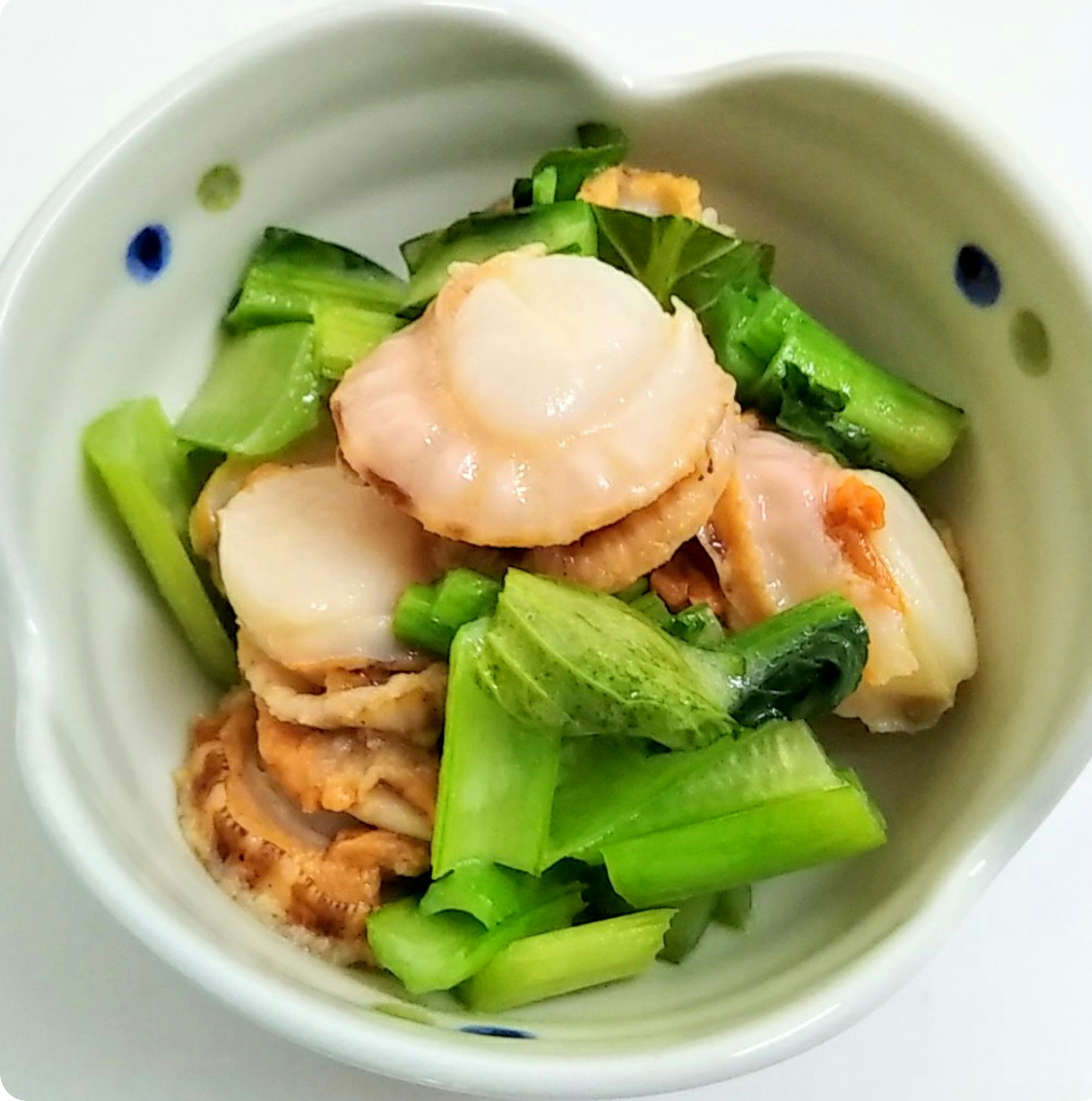 Dish of scallops and green vegetables in a white bowl