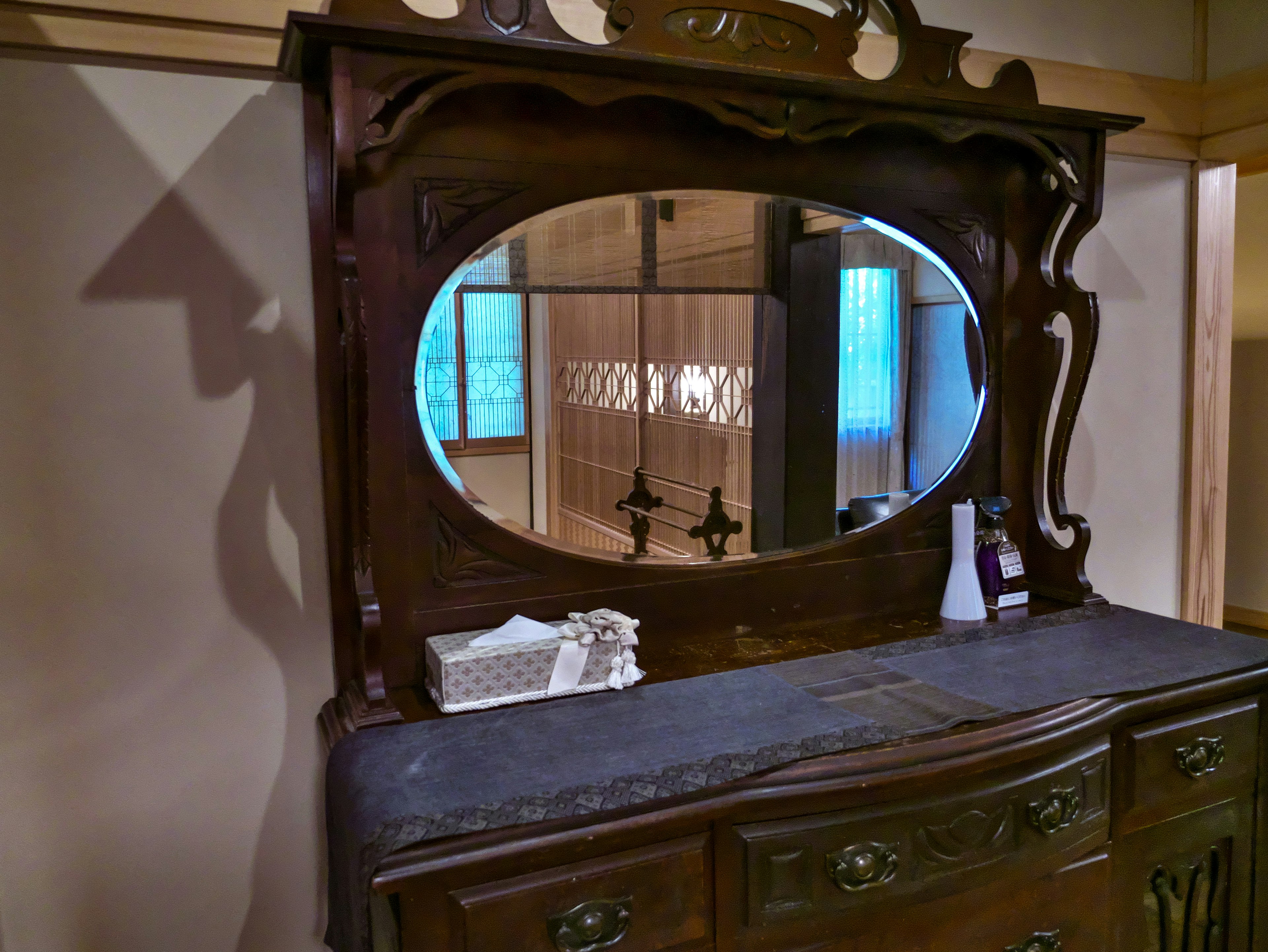 Antique wooden dresser with an oval mirror reflecting a room