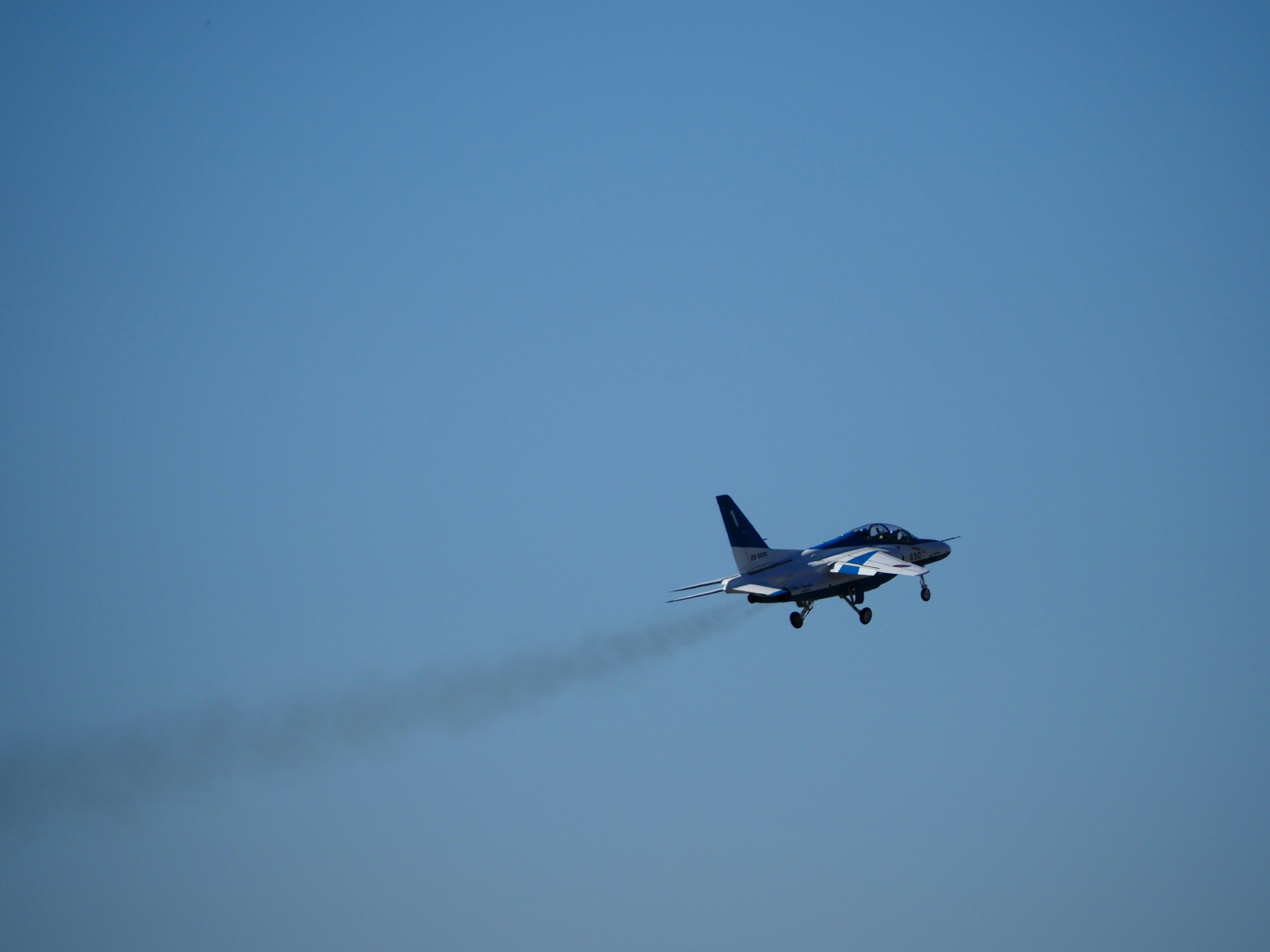 Un avion de chasse volant contre un ciel bleu laissant une traînée de fumée