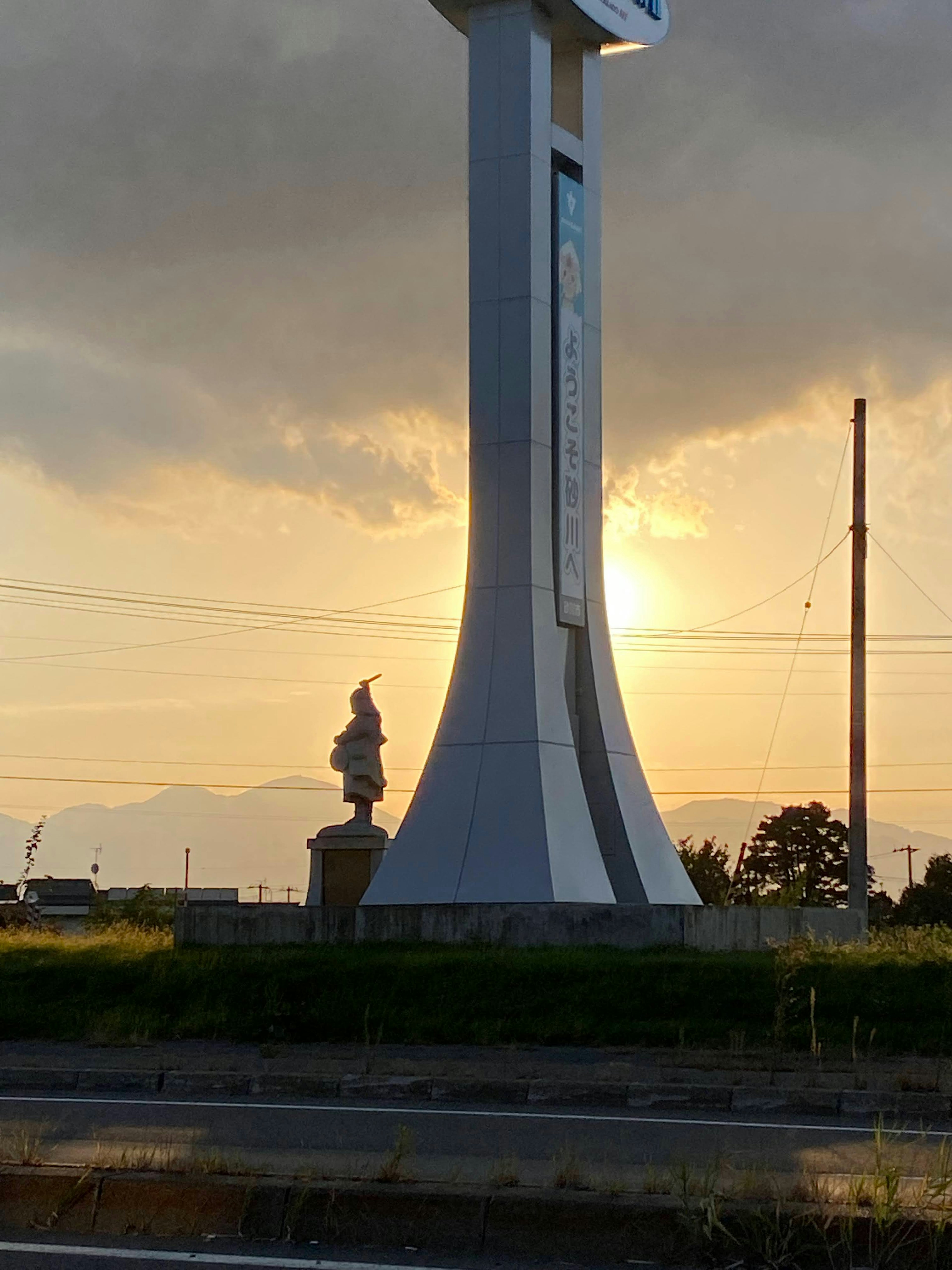 夕日を背景にした大きなモニュメントと小さな像