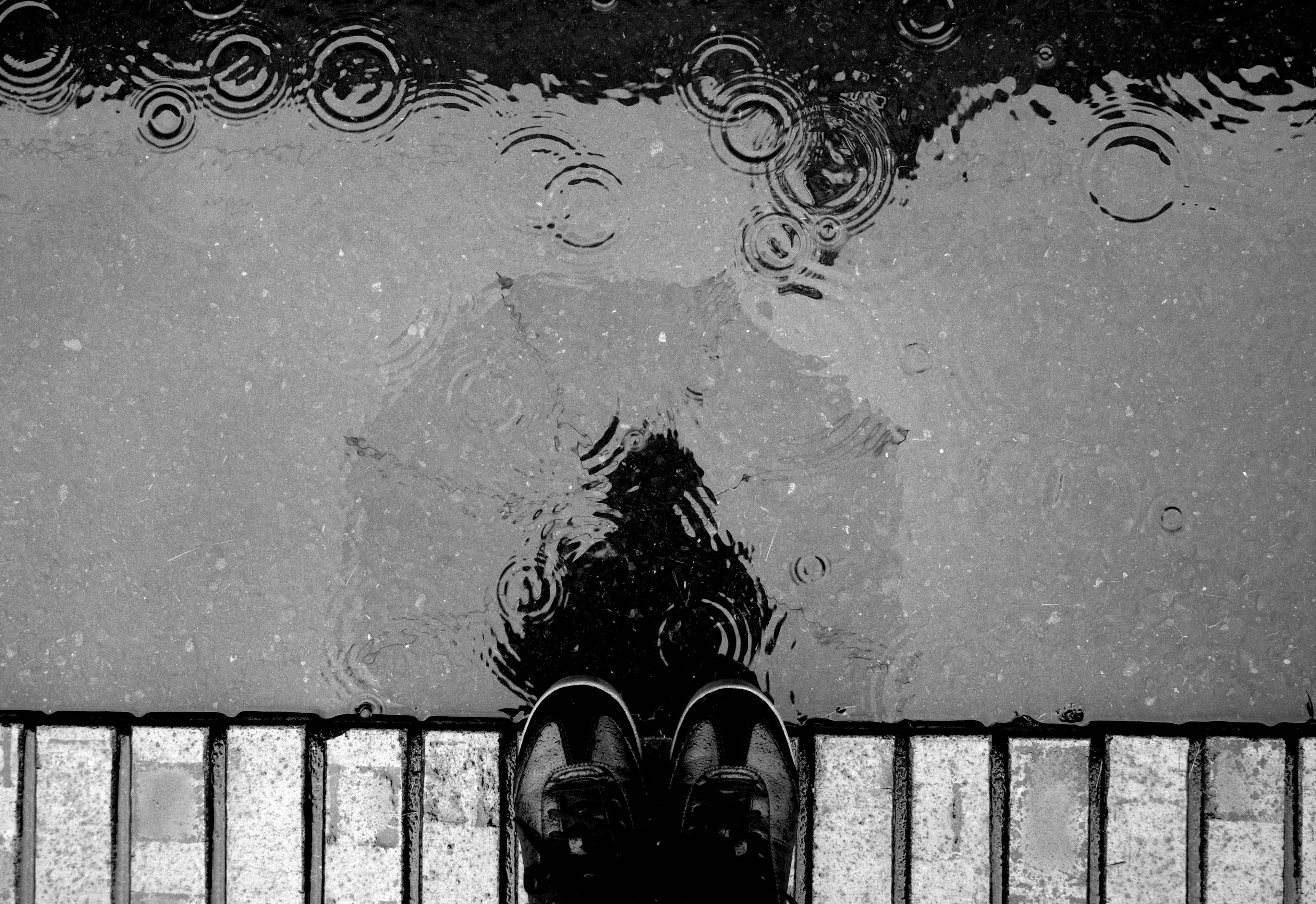 Imagen en blanco y negro de zapatos y reflejo de un paraguas en la lluvia