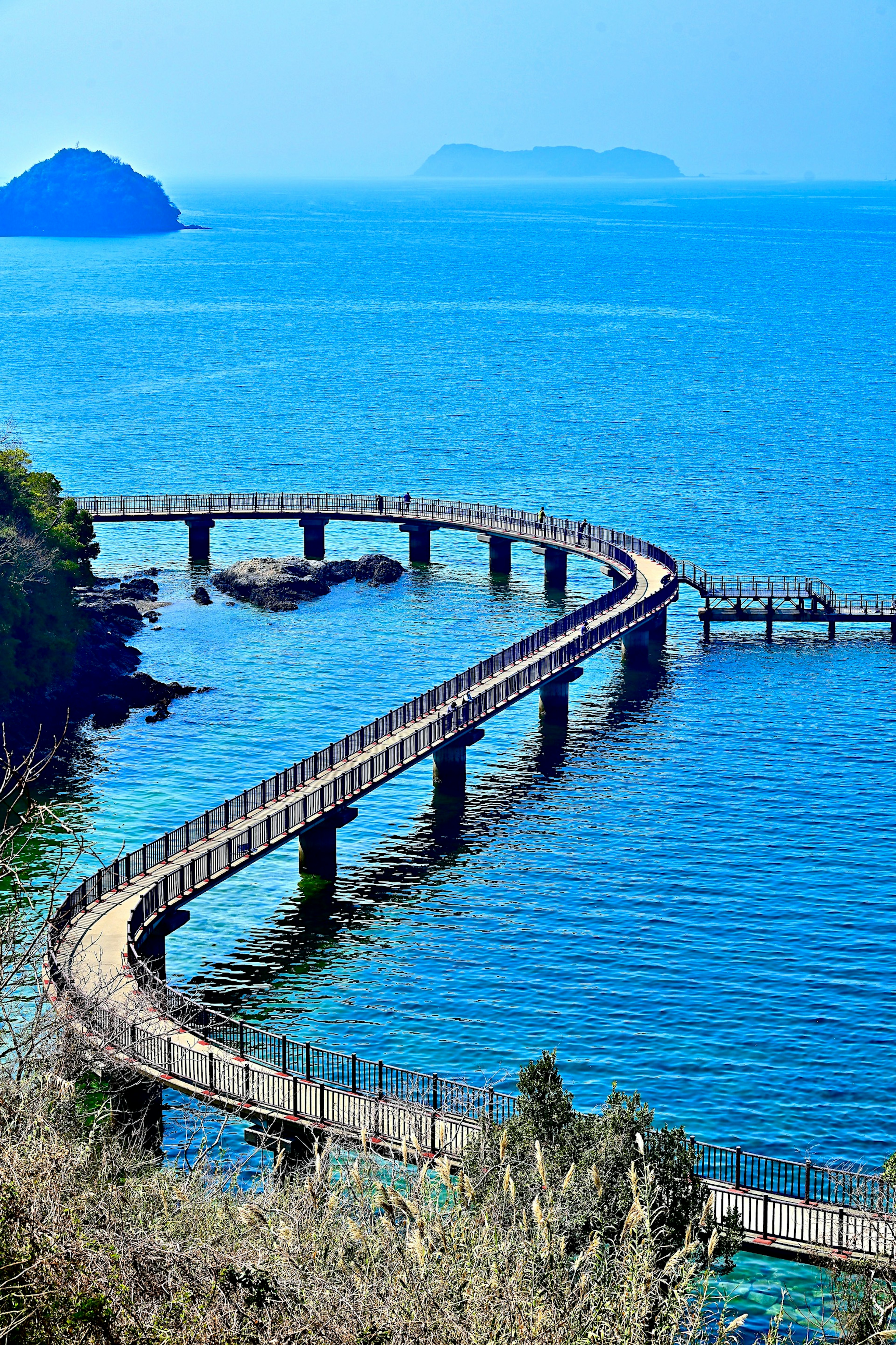 Jembatan kayu melengkung di sepanjang laut biru dengan pulau-pulau jauh