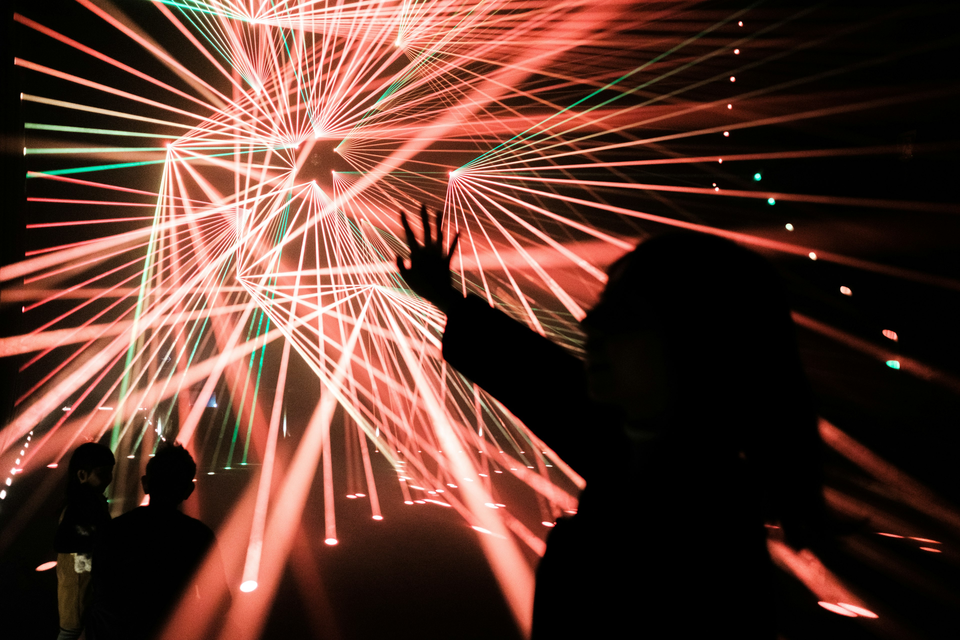 Silhouetten von Menschen, die die Hände heben, umgeben von bunten, sich kreuzenden Laserstrahlen