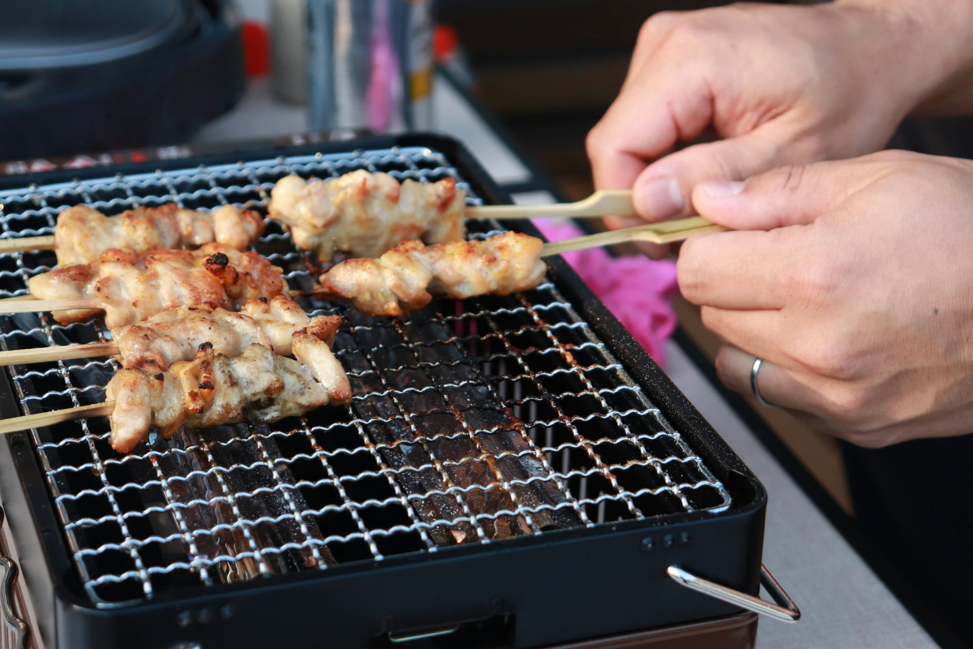 Hände, die Spieße mit gegrilltem Hähnchen auf einem Grill halten