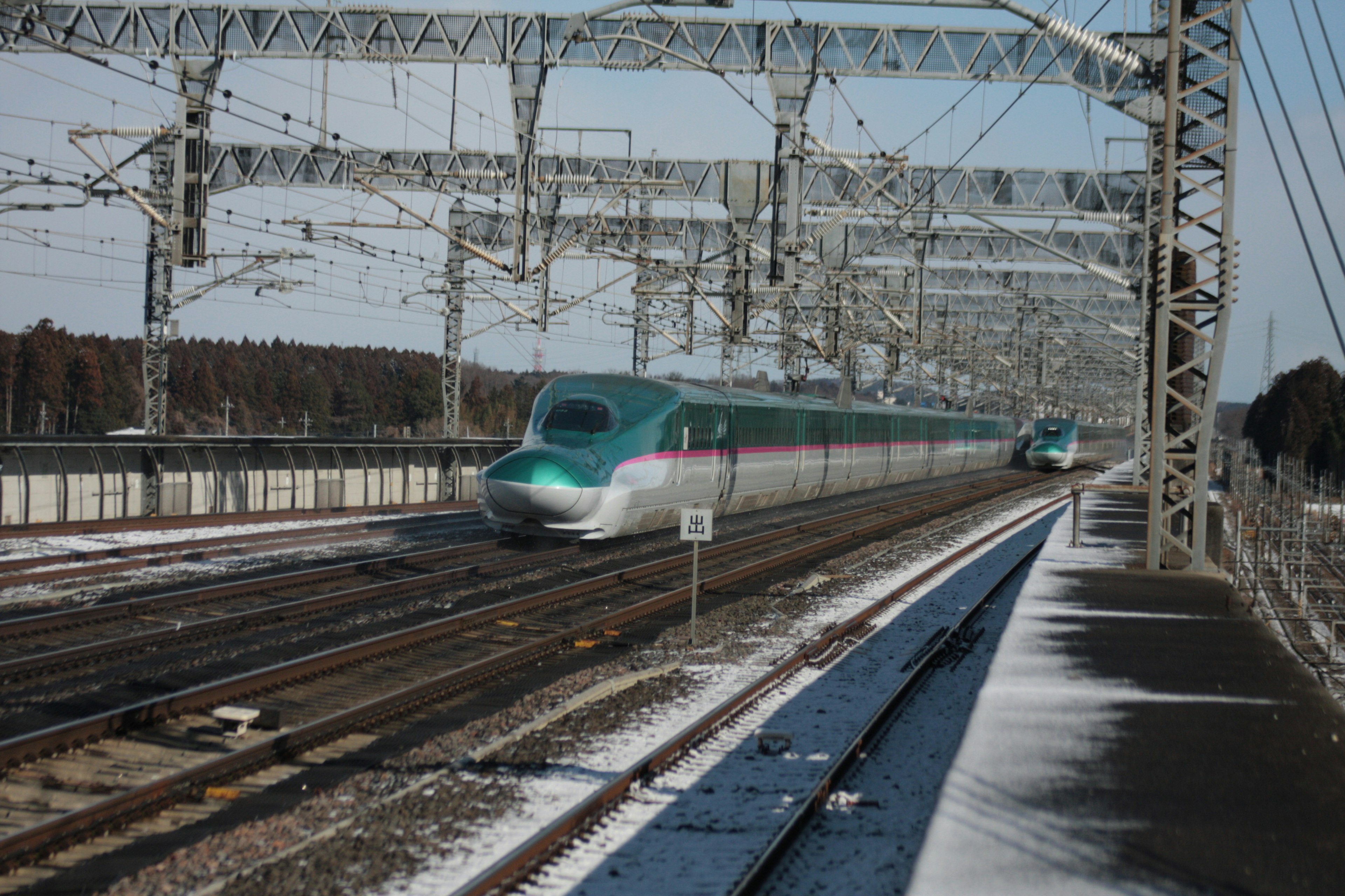 Shinkansen train speeding through snowy landscape with railway overhead wires