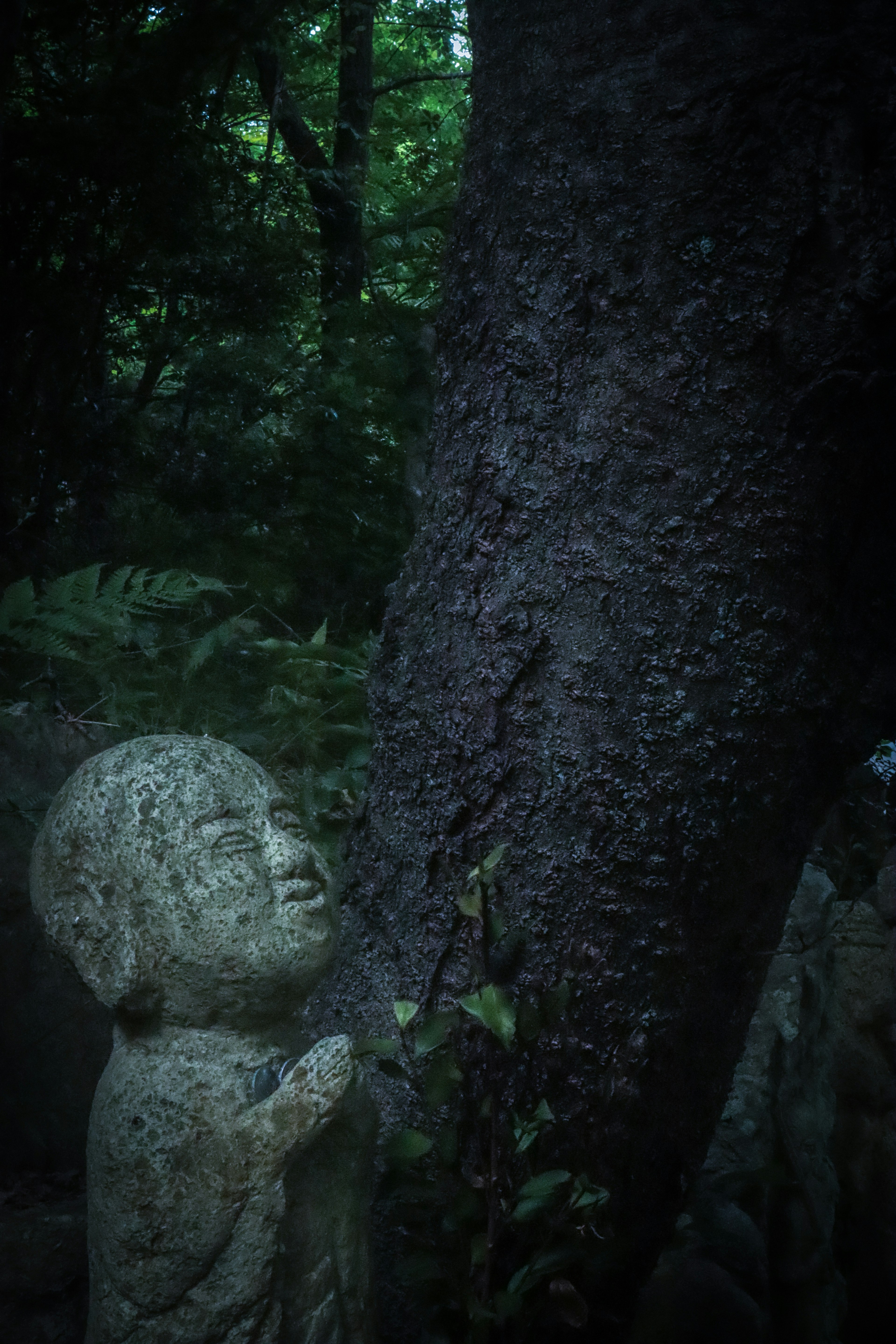 A small stone statue leaning against a tree in a dark forest