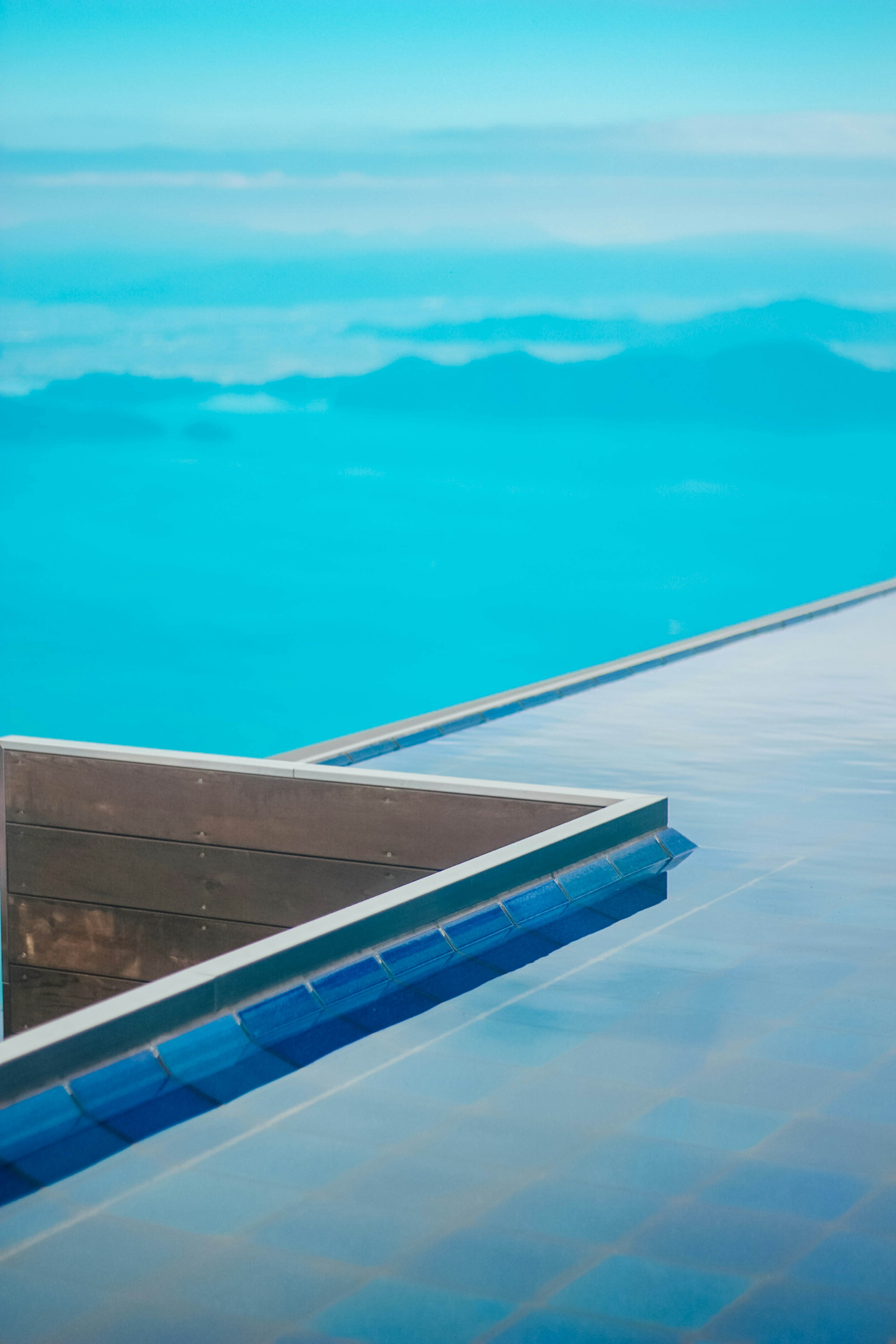 Coin d'une piscine reflétant le ciel bleu et les montagnes lointaines