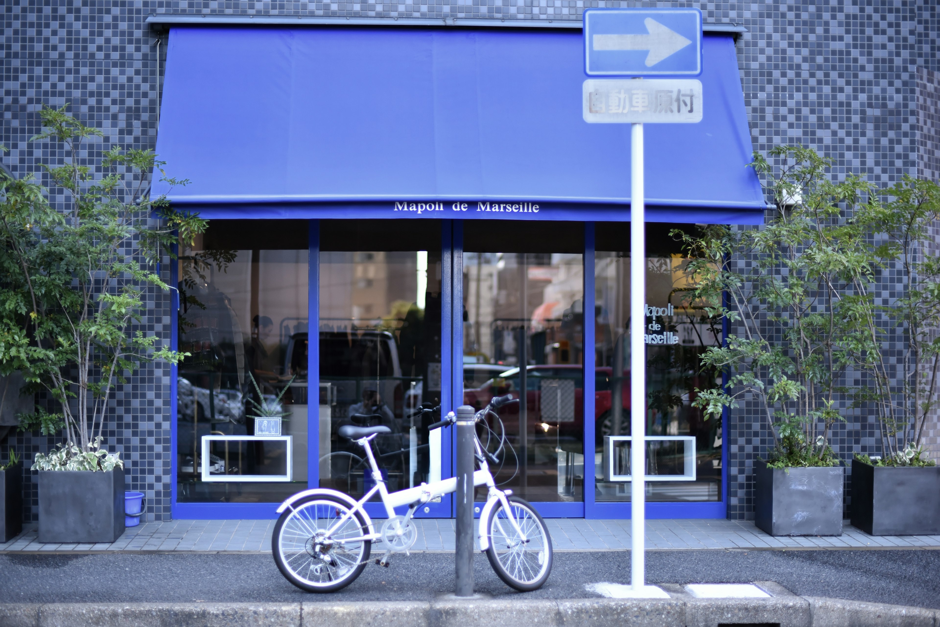 A white bicycle parked in front of a store with a blue awning