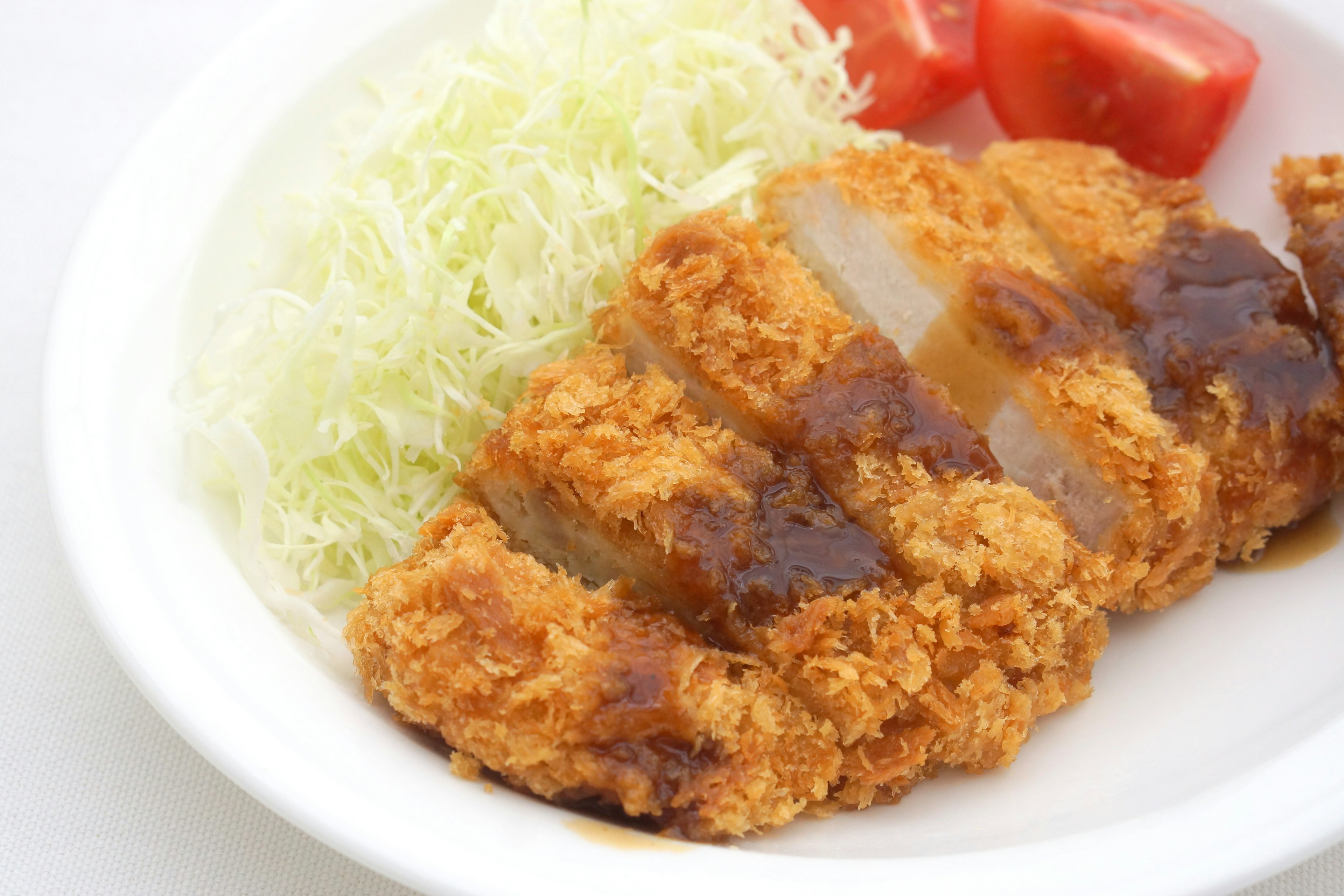 Breaded pork cutlet served with shredded cabbage and sliced tomatoes