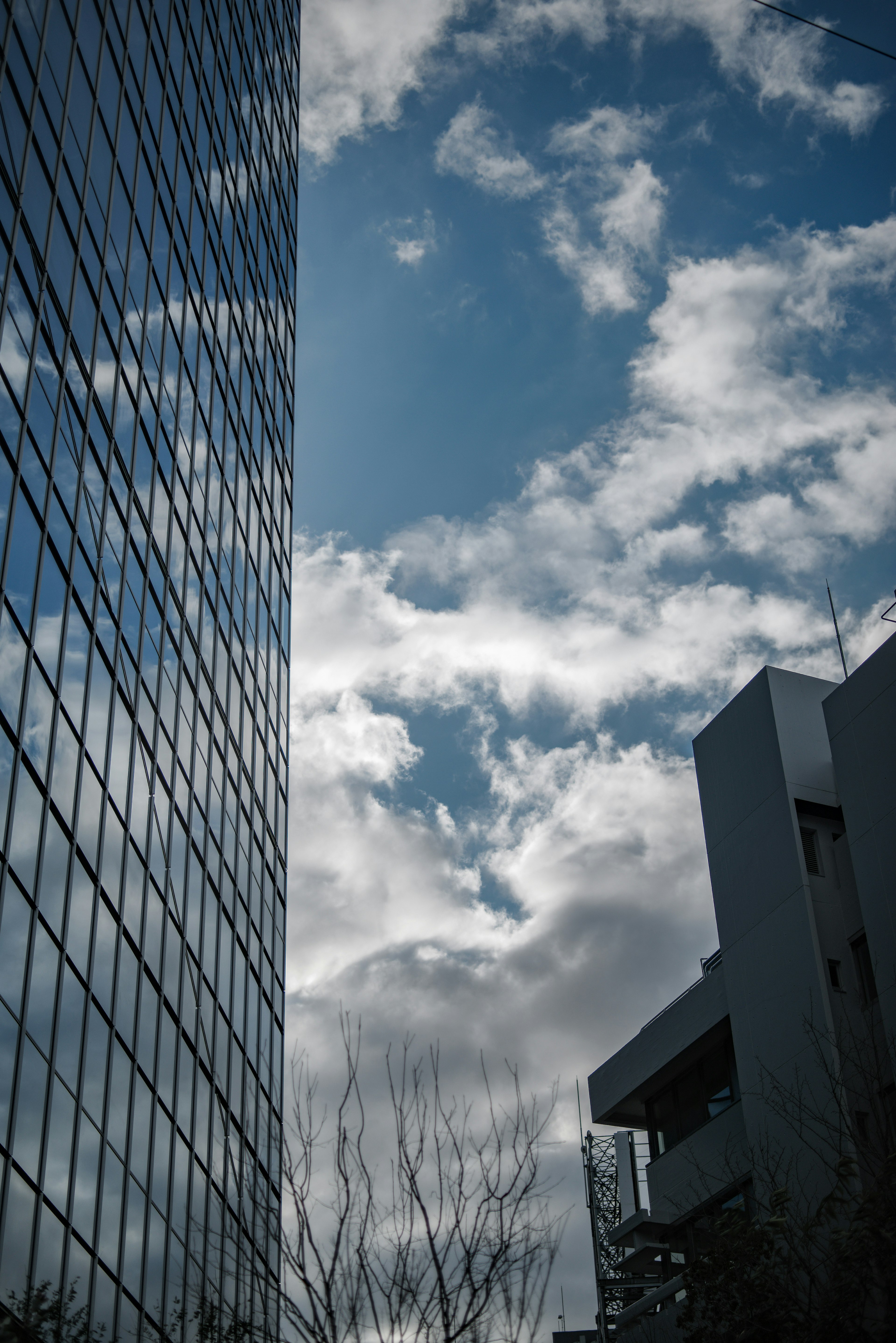 Glass wall of a skyscraper reflecting blue sky and clouds with nearby building