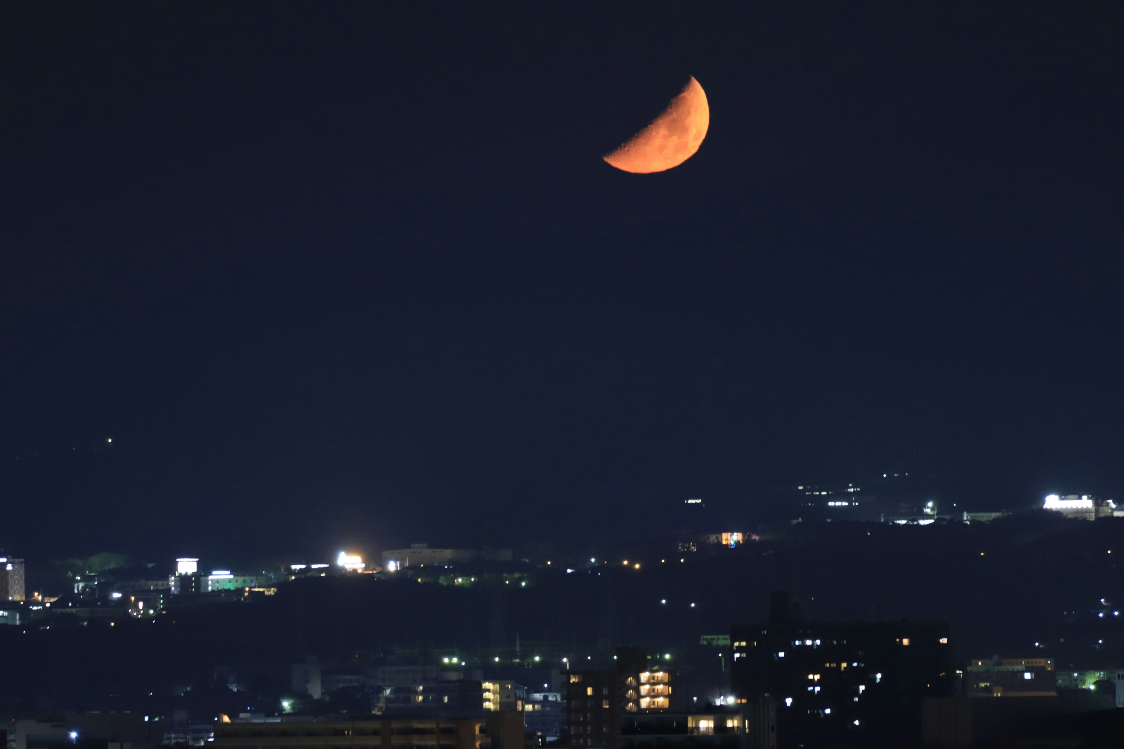 도시 불빛 위의 밤하늘에 떠 있는 오렌지색 초승달