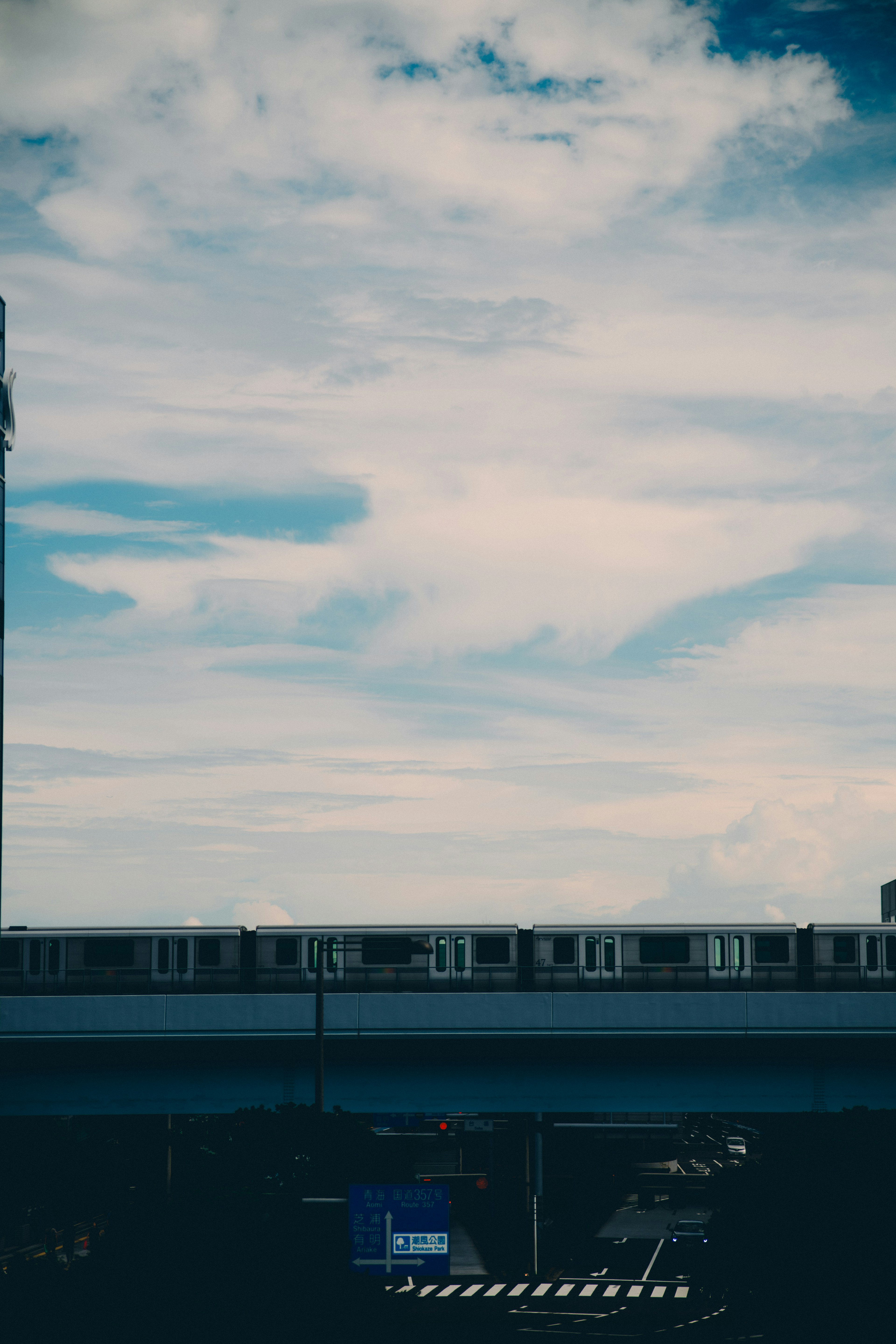 青空と白い雲の下を走るモノレールの風景