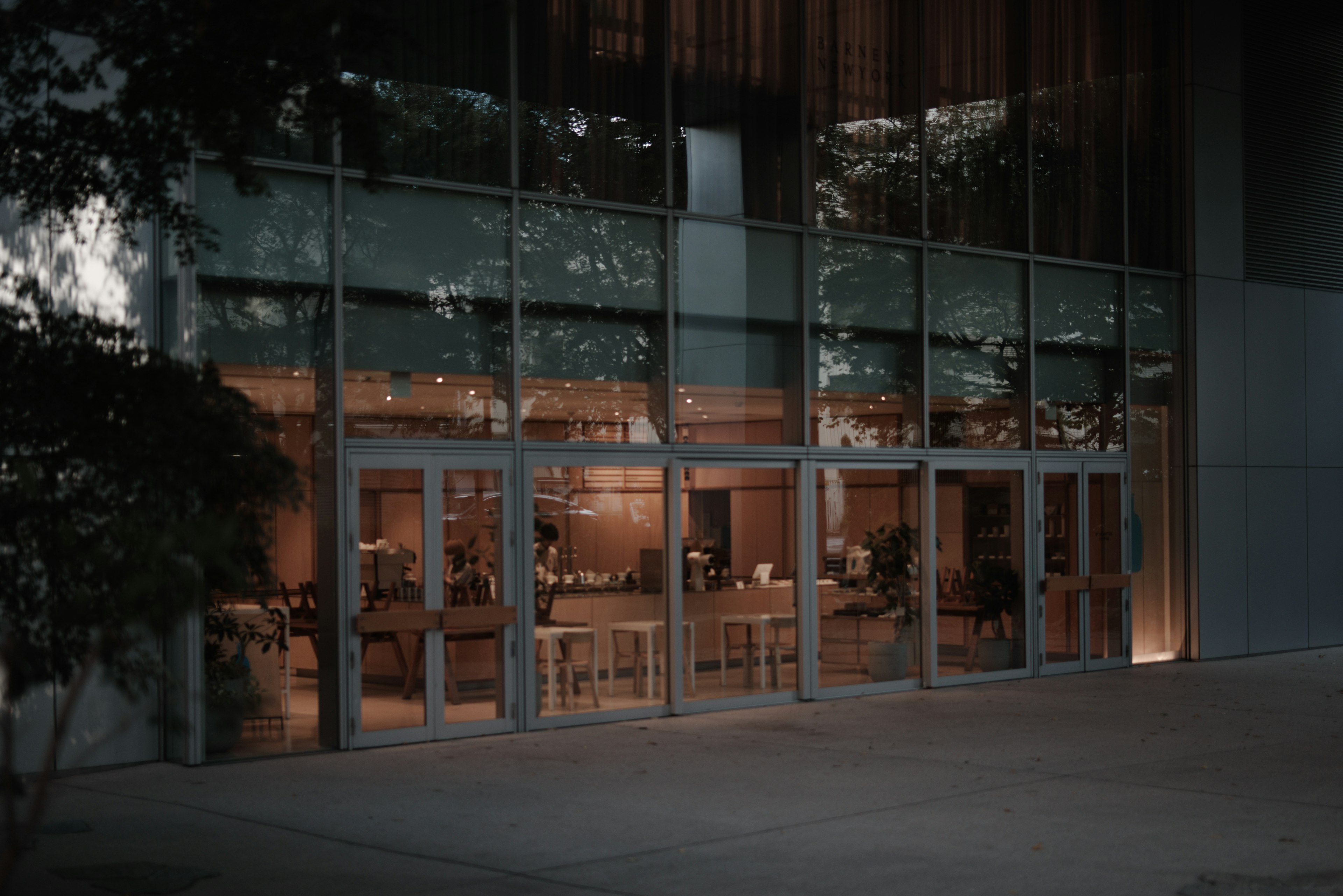 Night view of a cafe interior visible through a glass entrance of a building