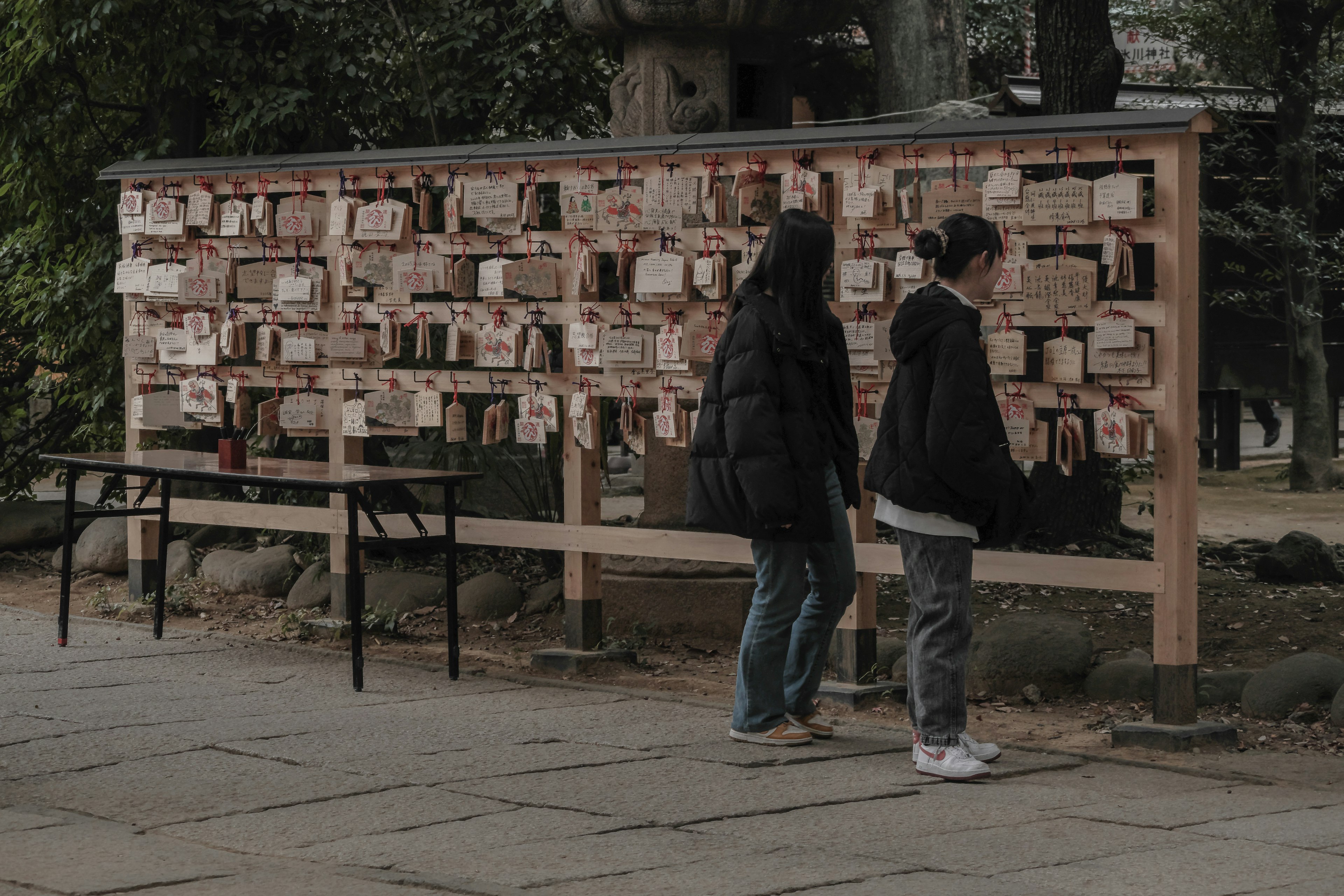 Two people walking in front of a wall of wooden ema plaques