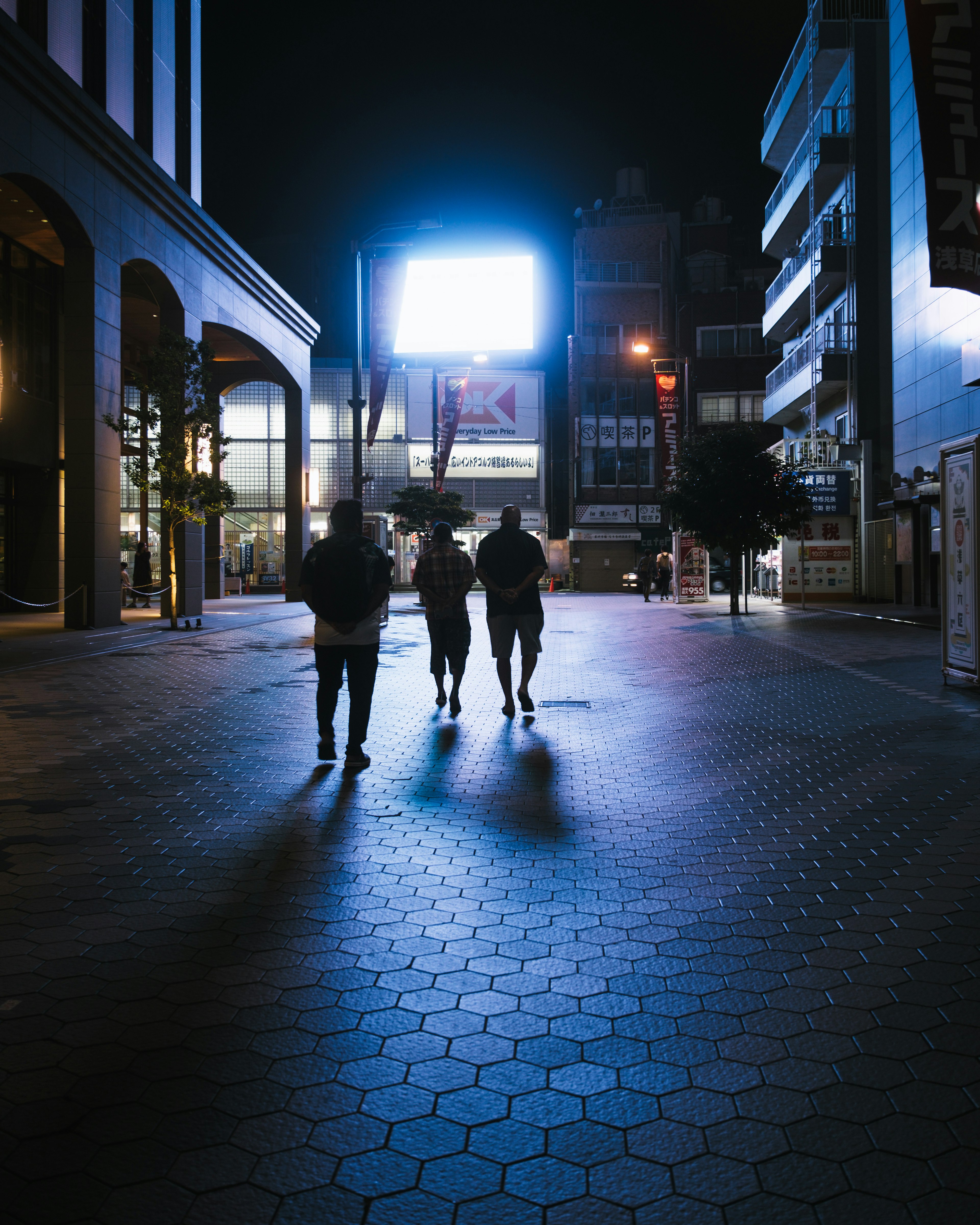 Silhouettes of people walking at night with blue light from a billboard