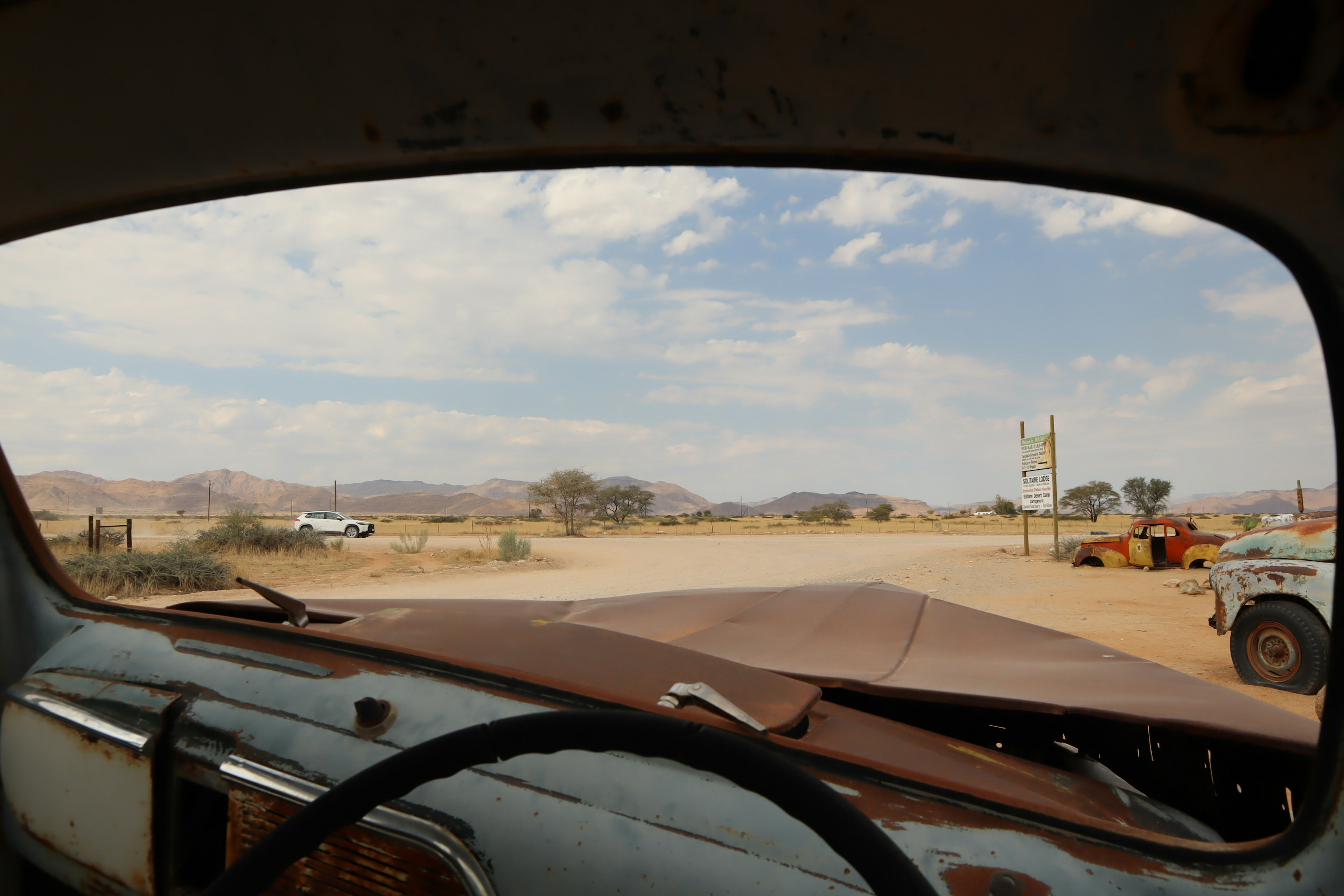 View from the driver's seat of an old car showing a dry landscape with mountains and blue sky