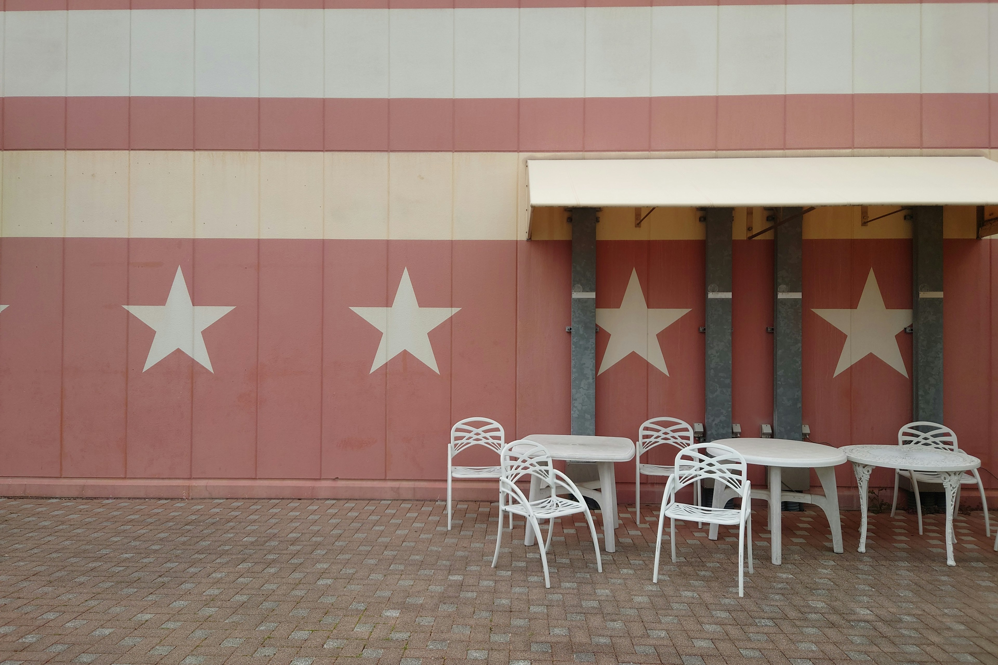 Espace extérieur avec des chaises et une table blanches contre un mur rayé rouge et blanc avec des étoiles