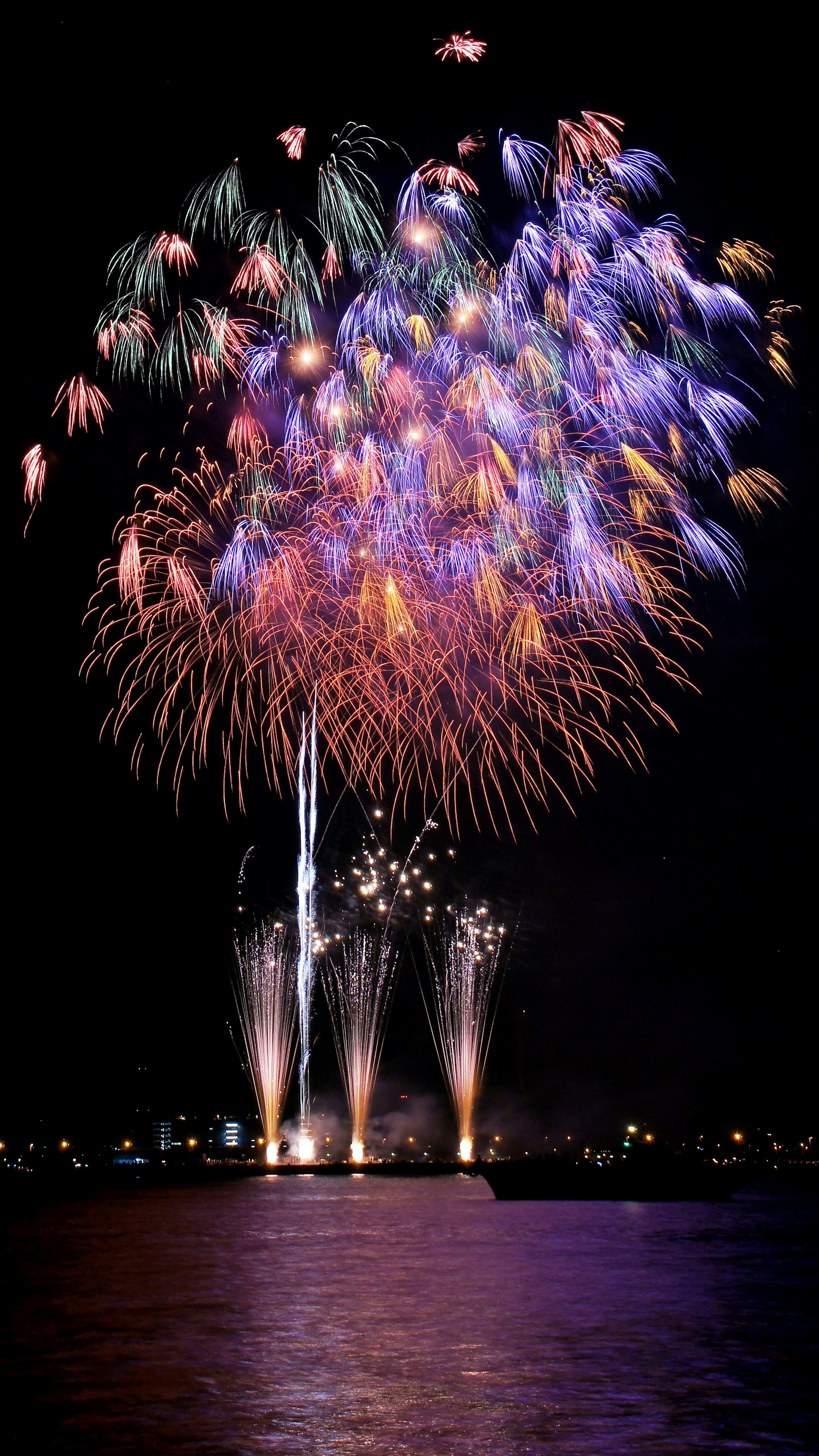 Colorful fireworks burst in the night sky reflecting on the water surface