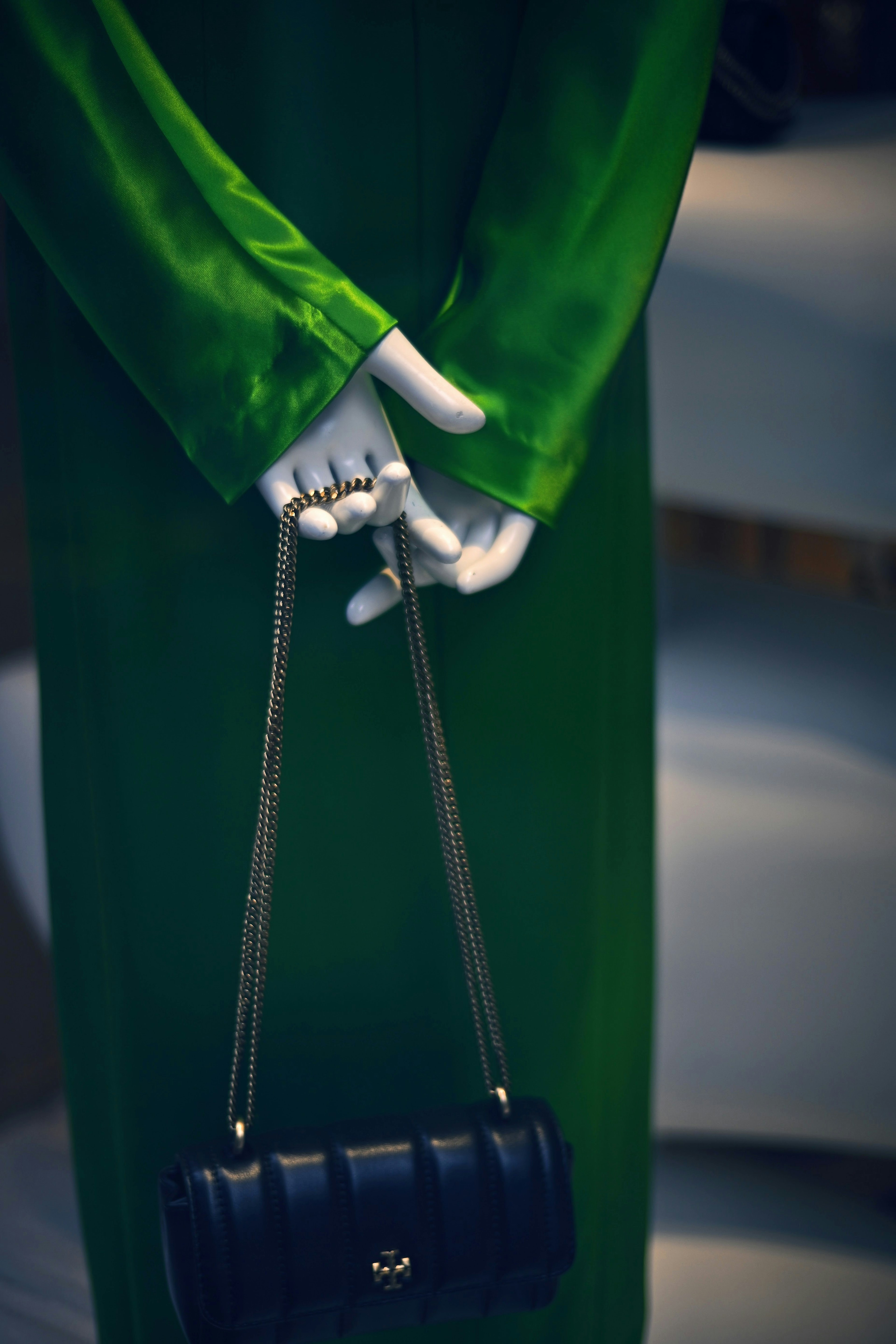 A mannequin wearing a green dress holding a black handbag