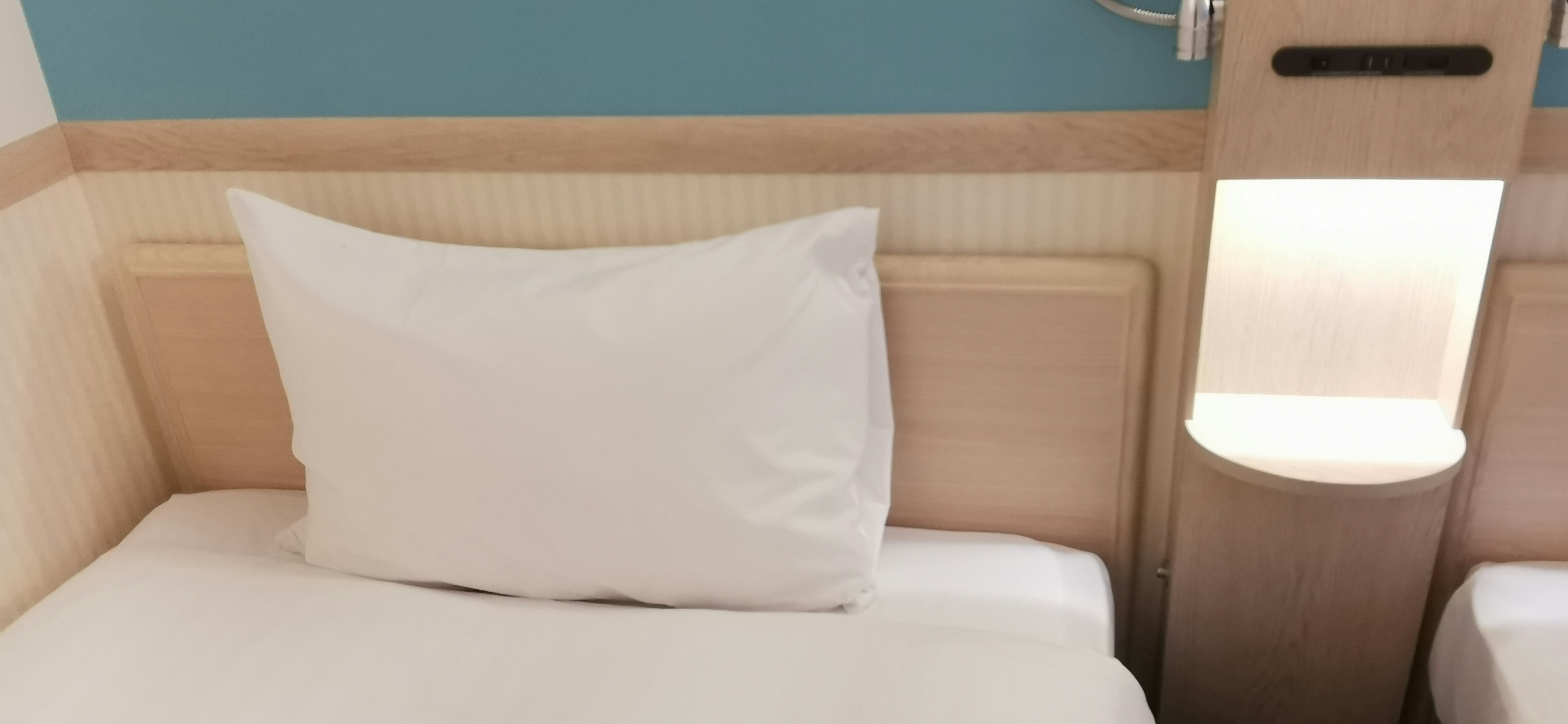 A simple bed with a white pillow featuring a blue wall and wooden headboard