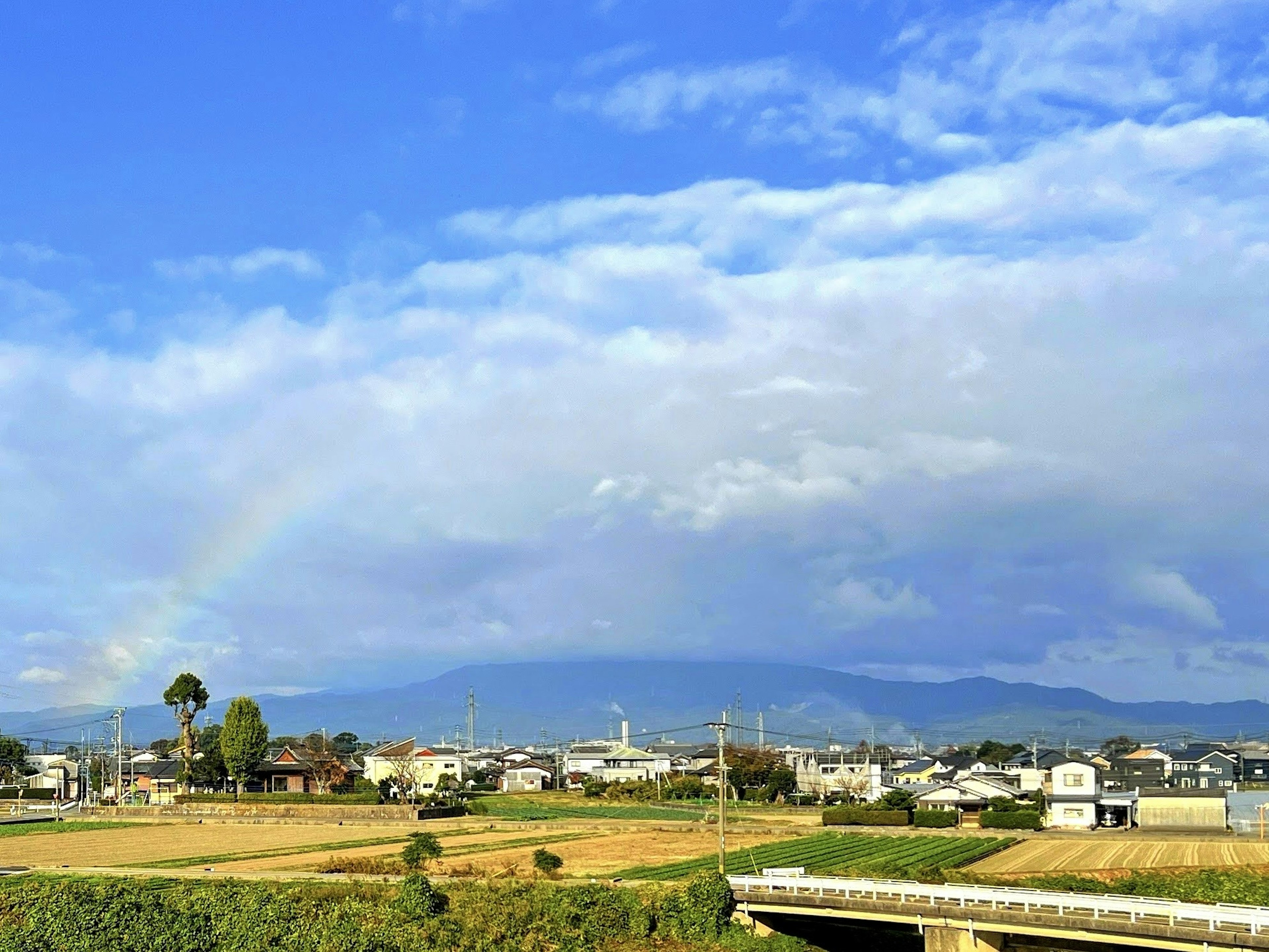 Paysage rural sous un ciel bleu avec des nuages et un arc-en-ciel