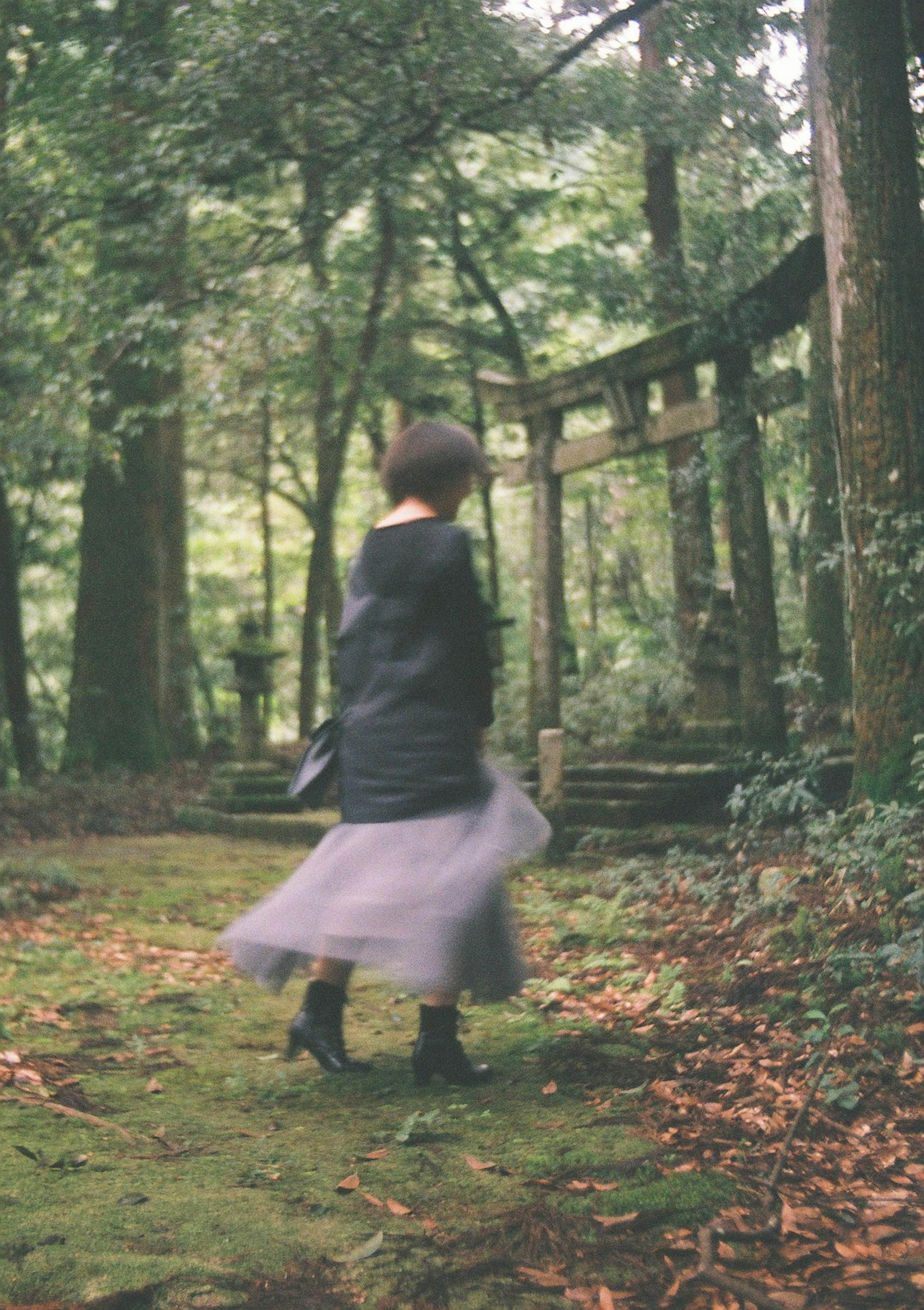 A woman twirling in a forest with a torii gate in the background