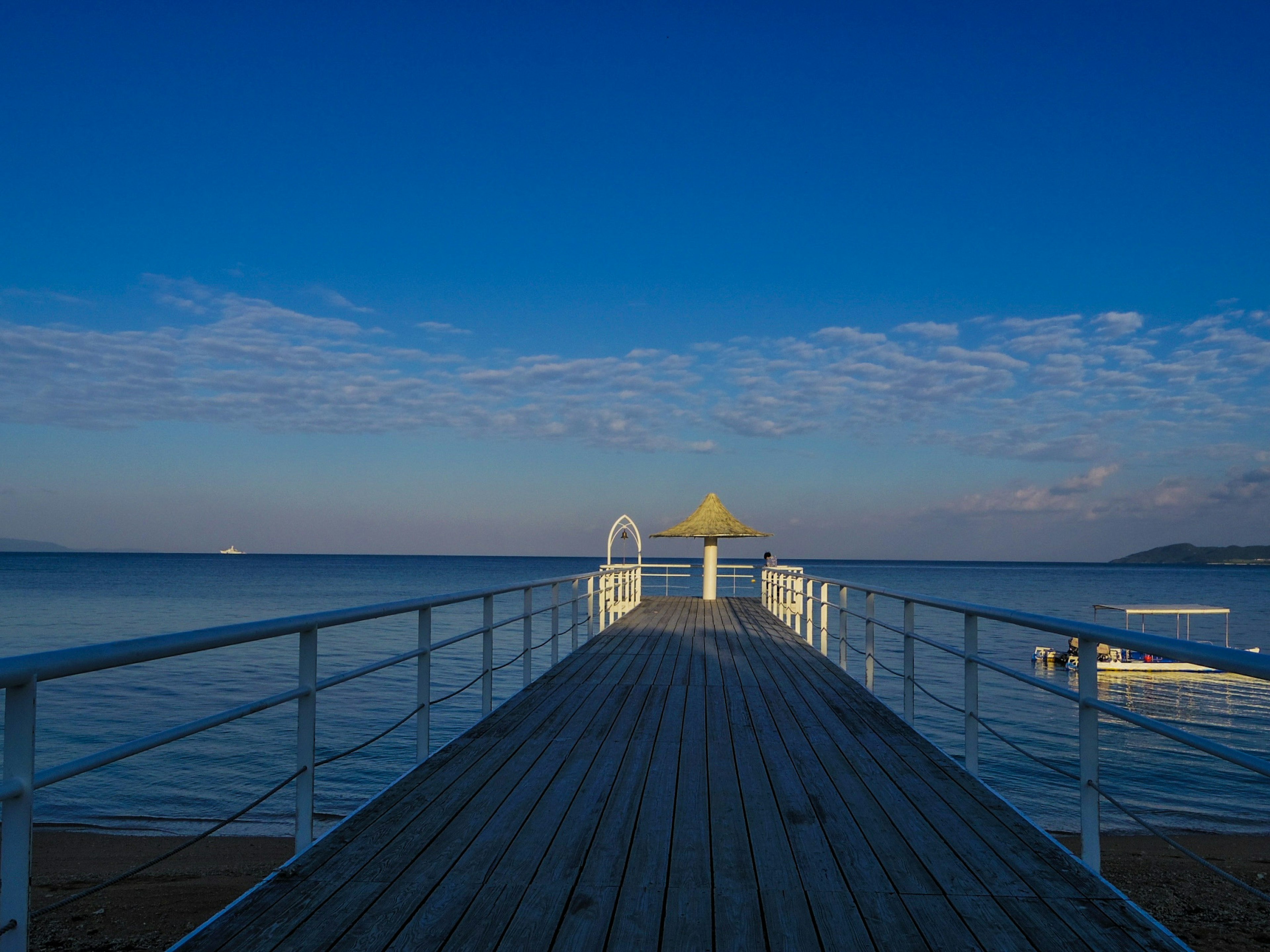 Weißer Steg, der ins Meer unter einem blauen Himmel mit Wolken führt