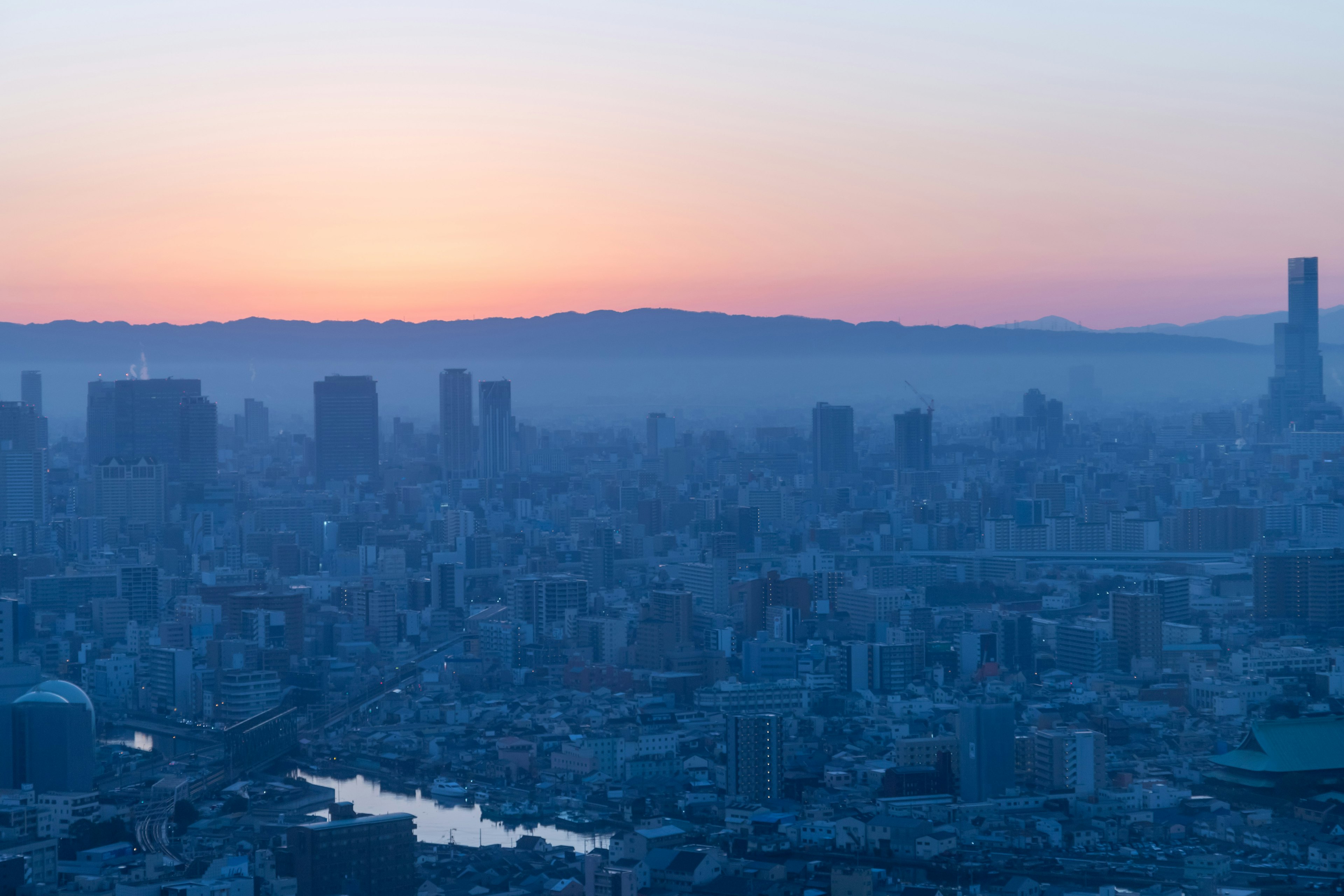 Paisaje urbano al atardecer con tonos azules y siluetas de montañas