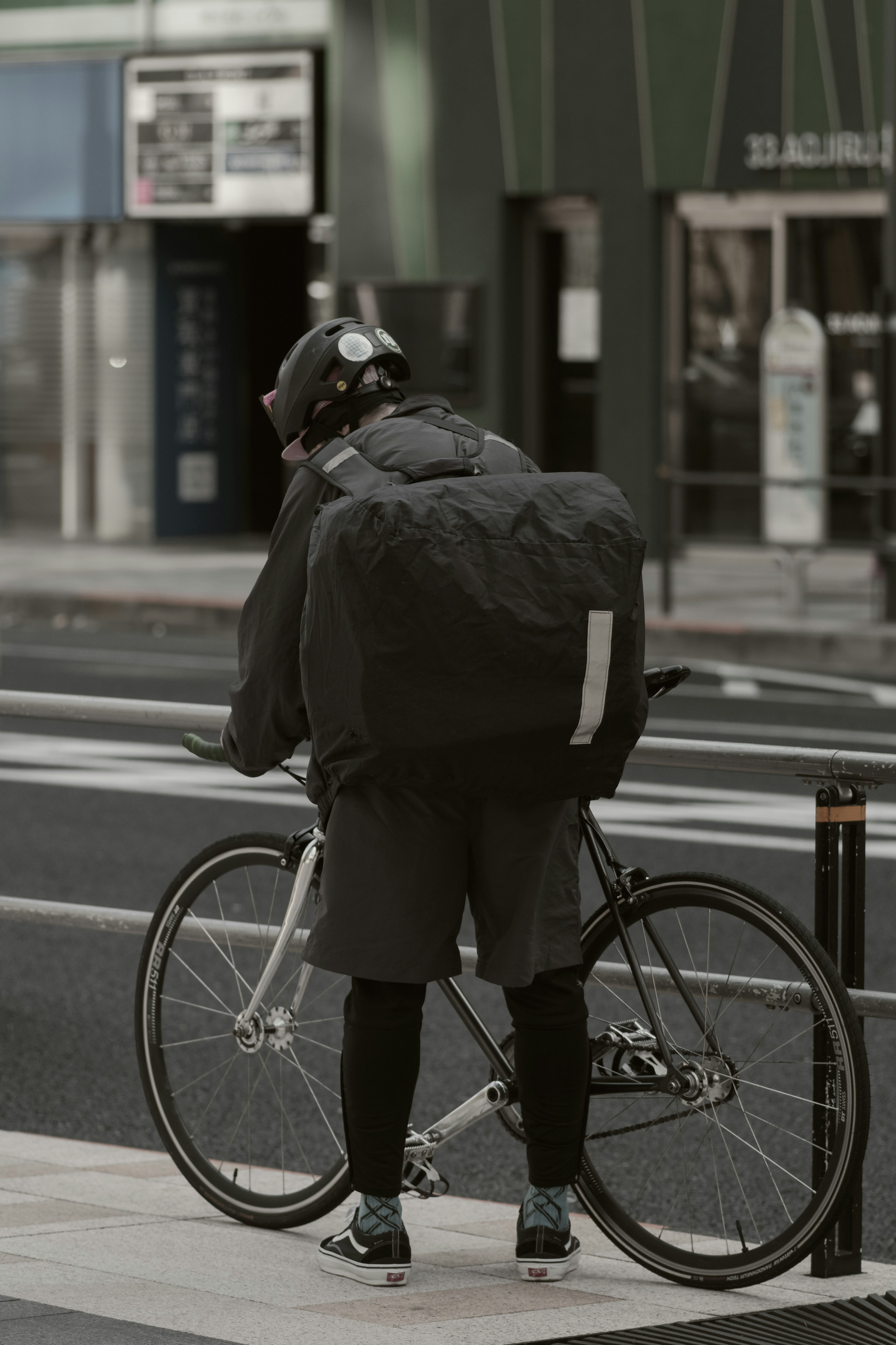 Corriere con cuffie in piedi accanto a una bicicletta in una strada cittadina