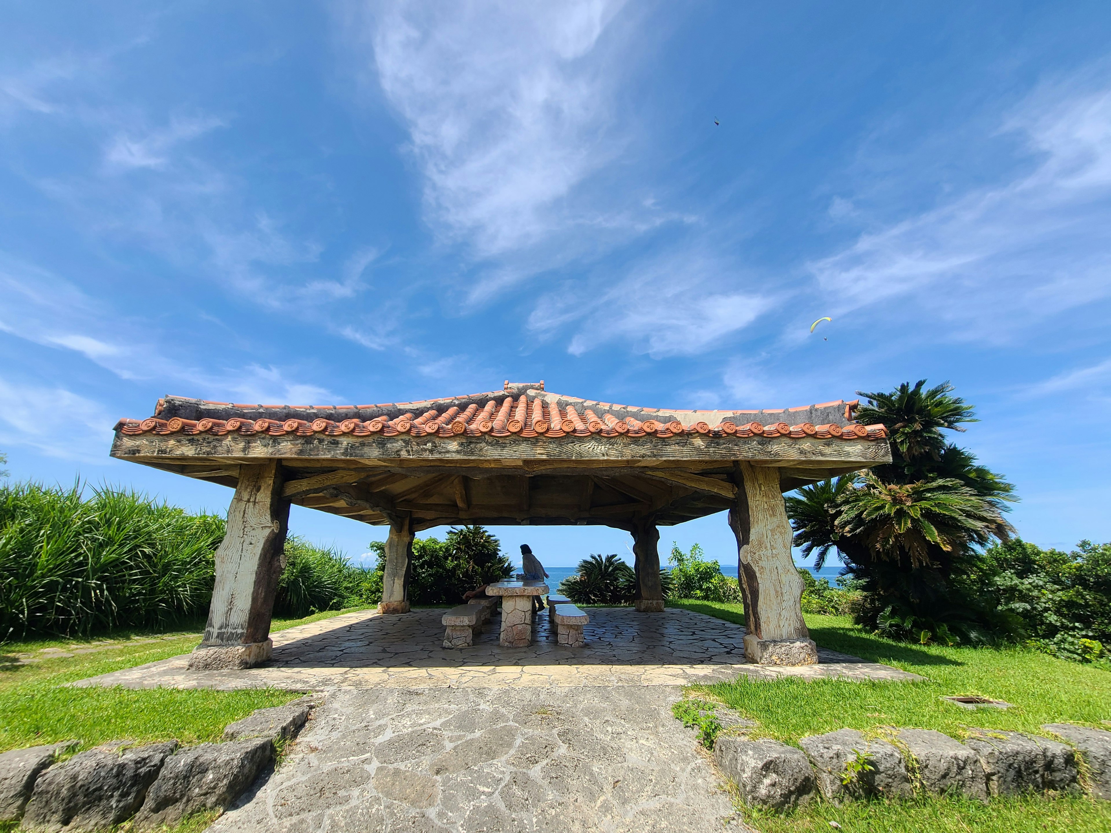 Traditional roofed pavilion under a blue sky surrounded by lush greenery