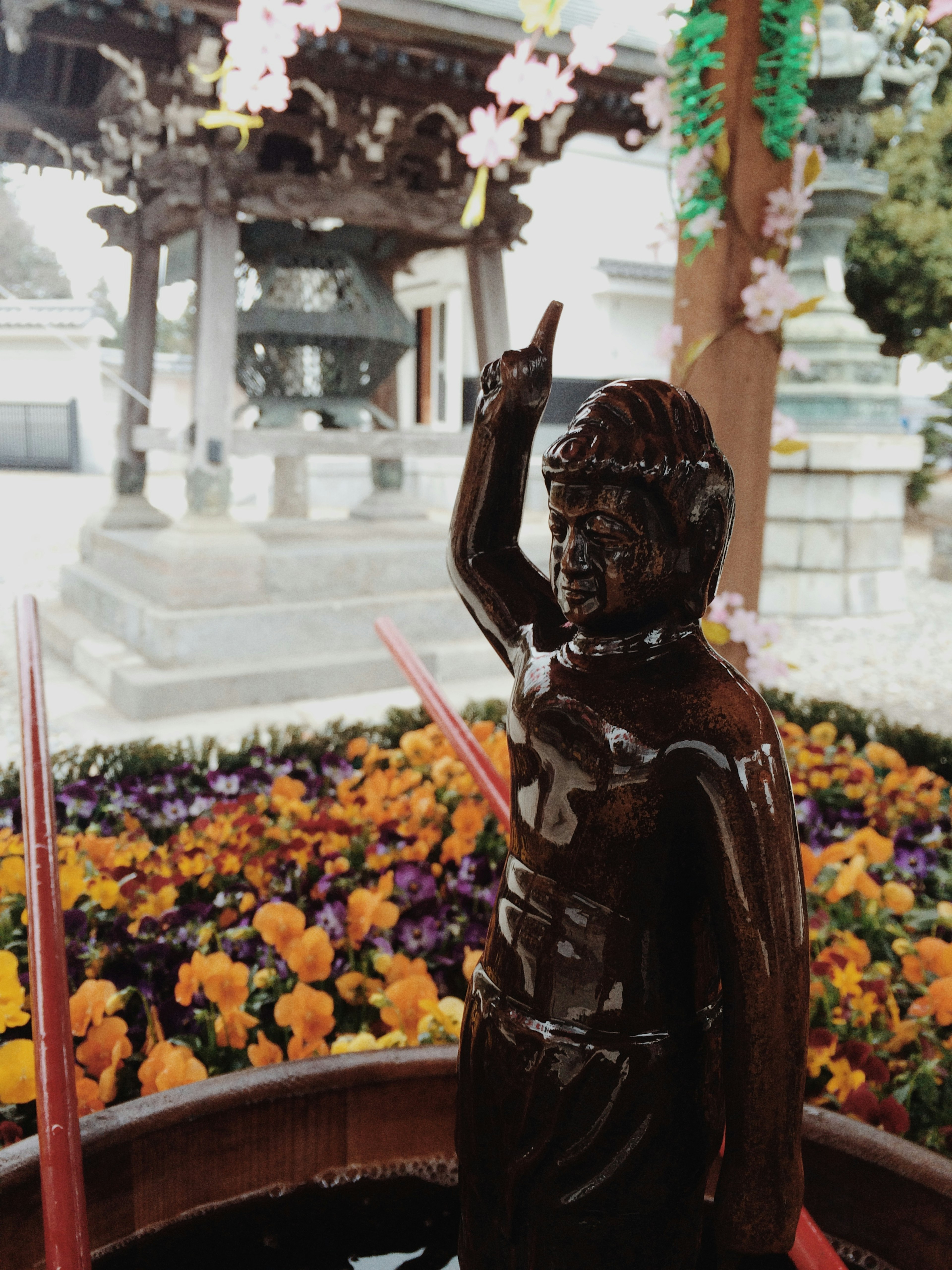 水を注ぐための銅像と色とりどりの花がある寺院の景観