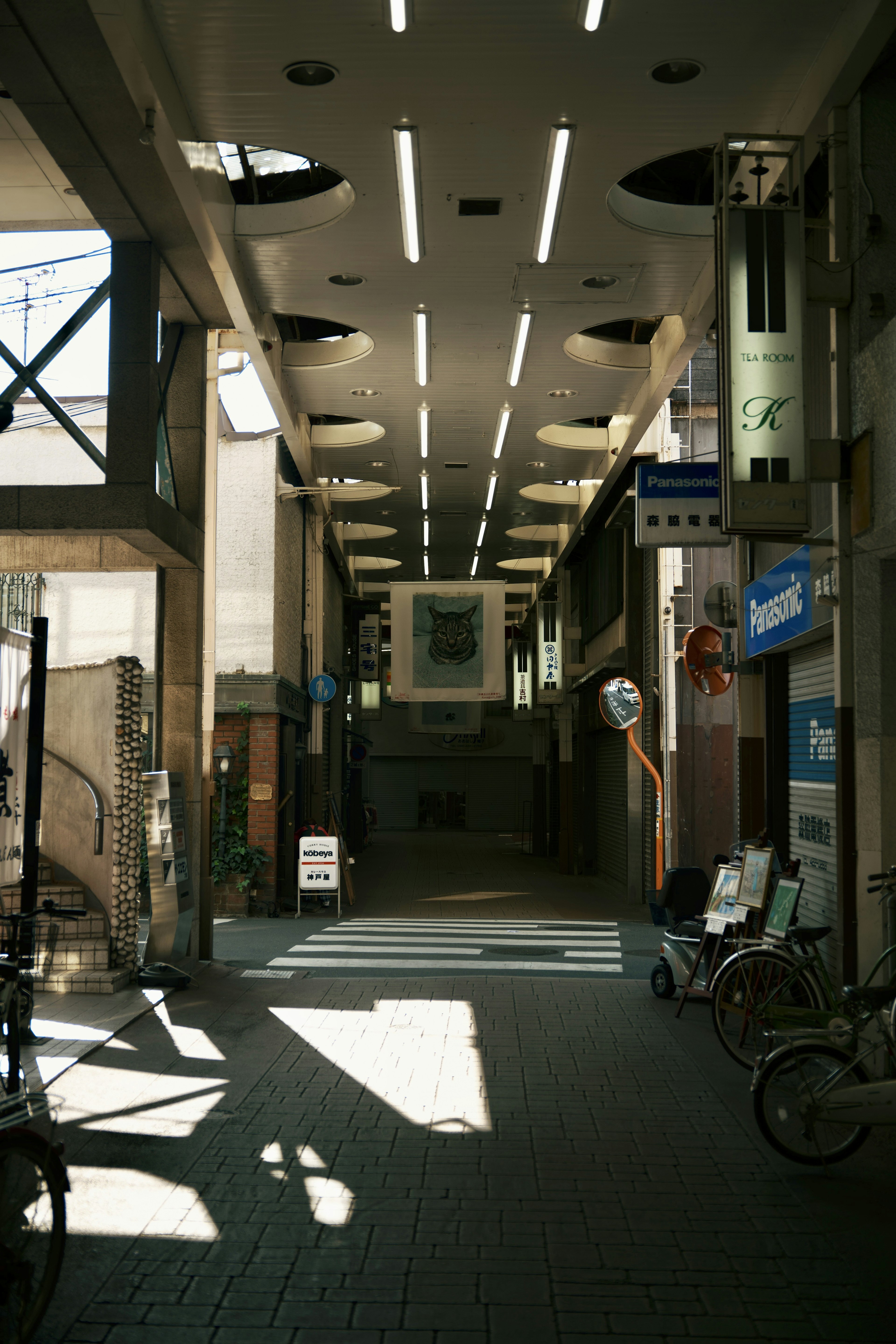 A bright corridor leading through a shopping arcade with bicycles parked nearby featuring striking lighting design