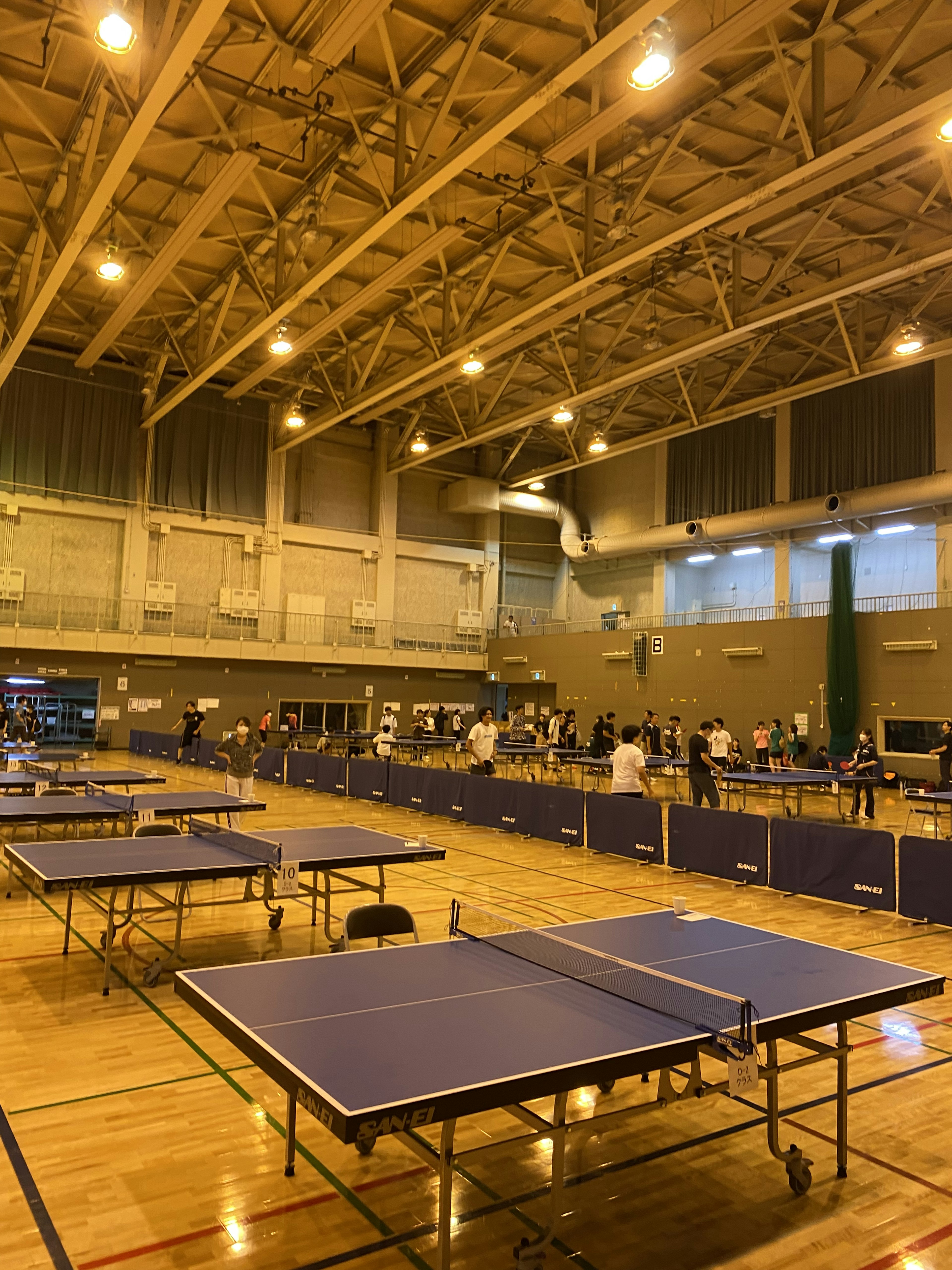 Gimnasium yang luas dengan deretan meja ping pong dan penonton