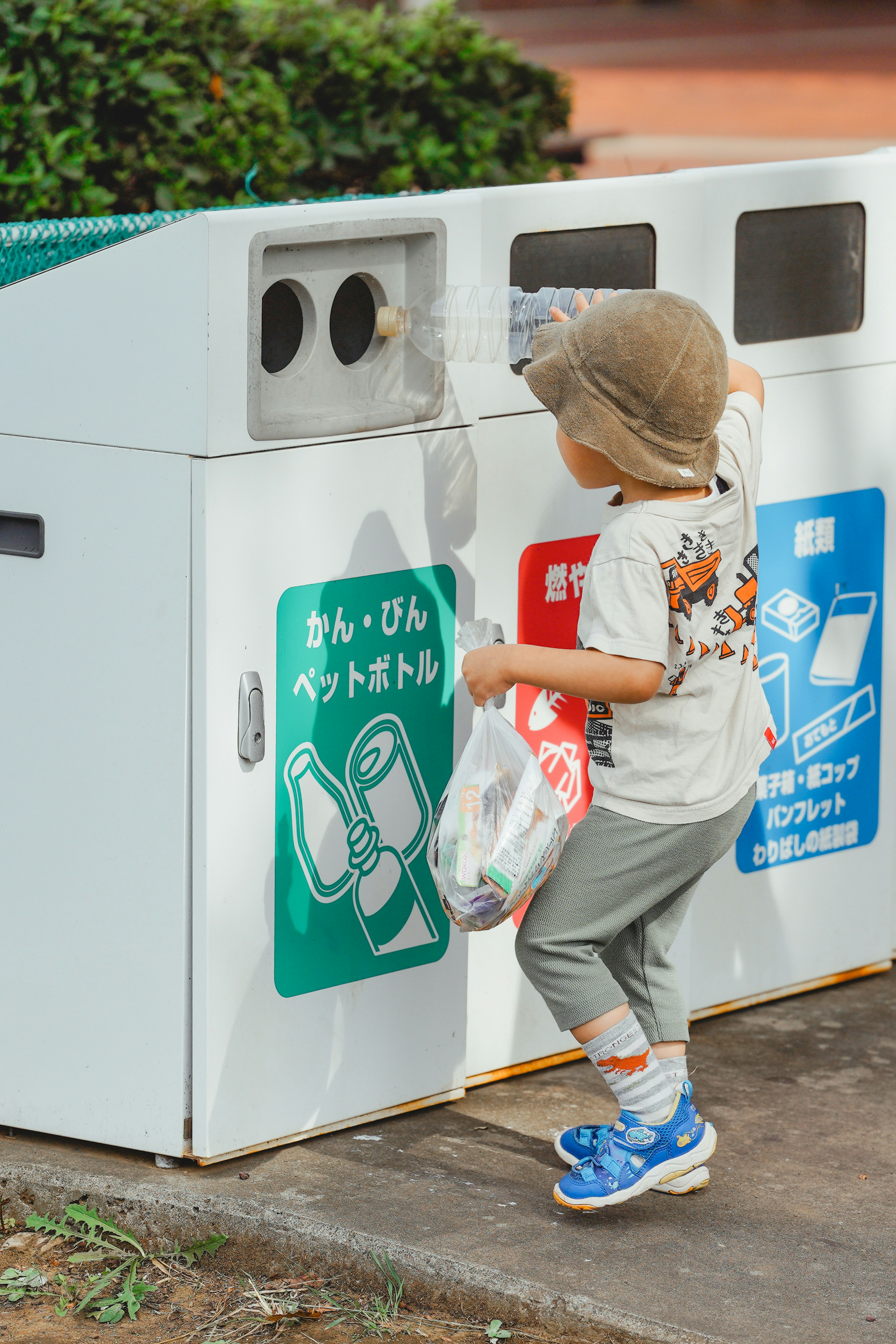 Seorang anak membuang barang daur ulang ke dalam tempat sampah dengan label berwarna