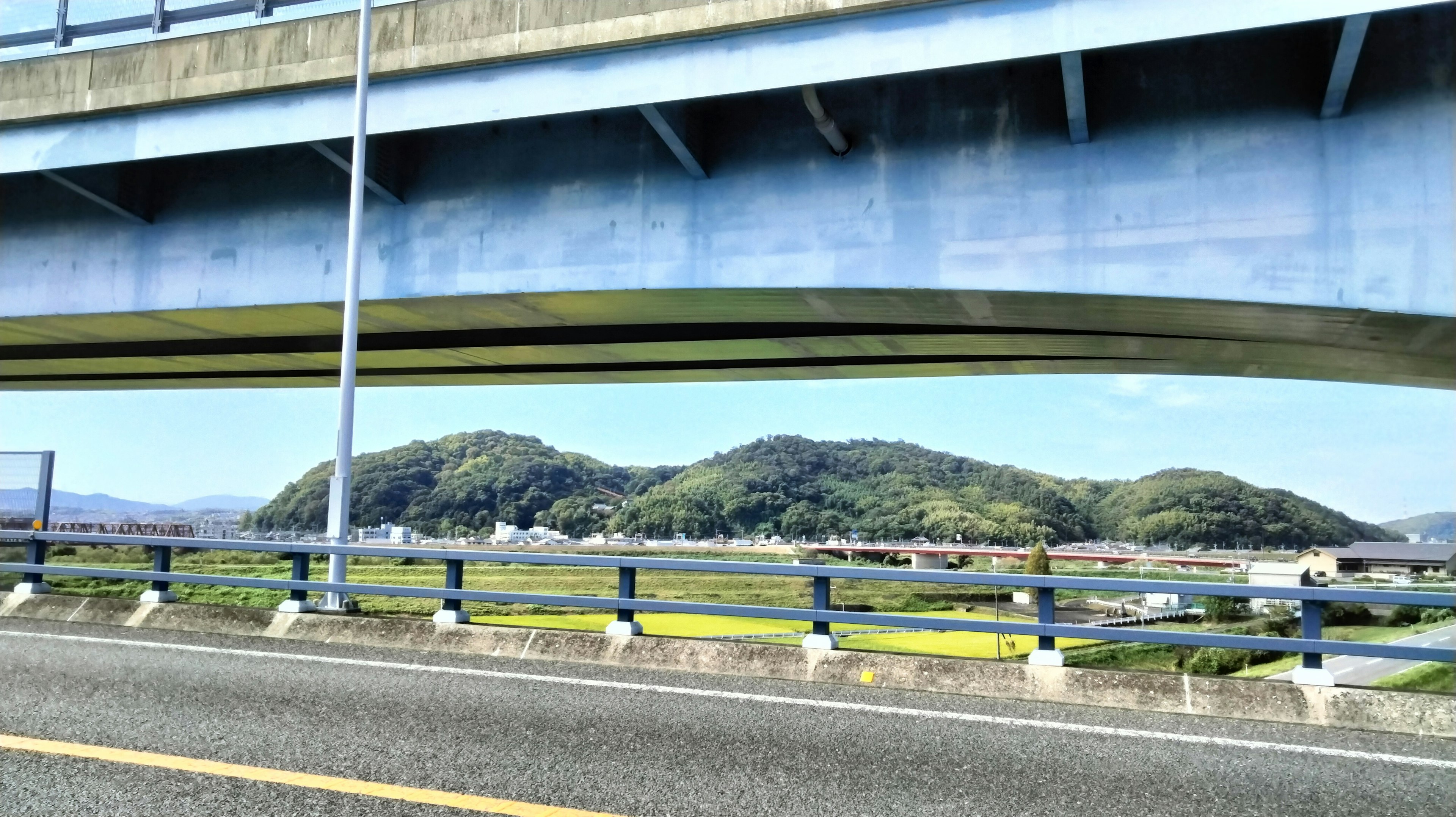 Bukit hijau dan langit biru terlihat di bawah jembatan biru