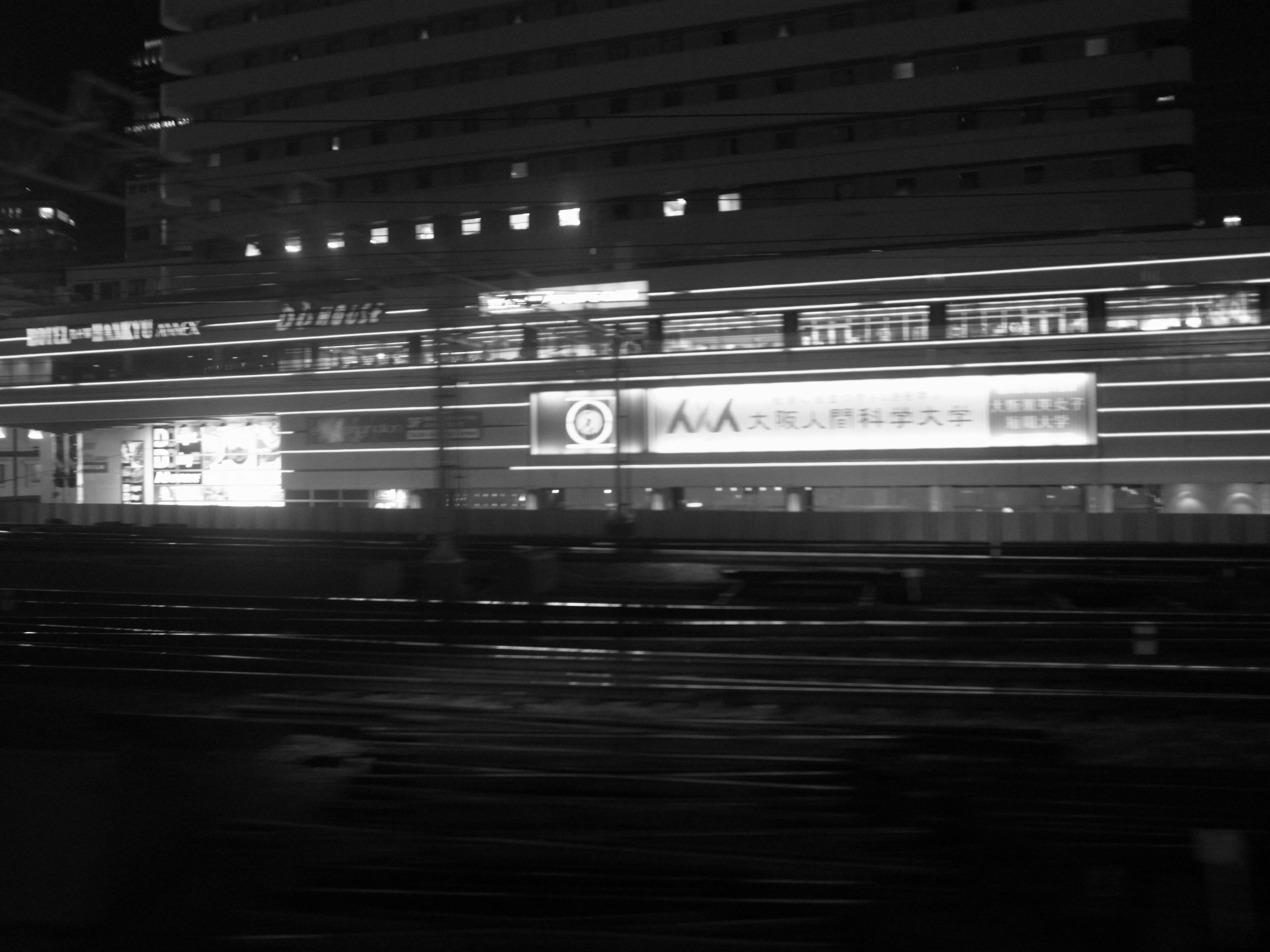 Black and white image of a moving train in a nighttime urban setting