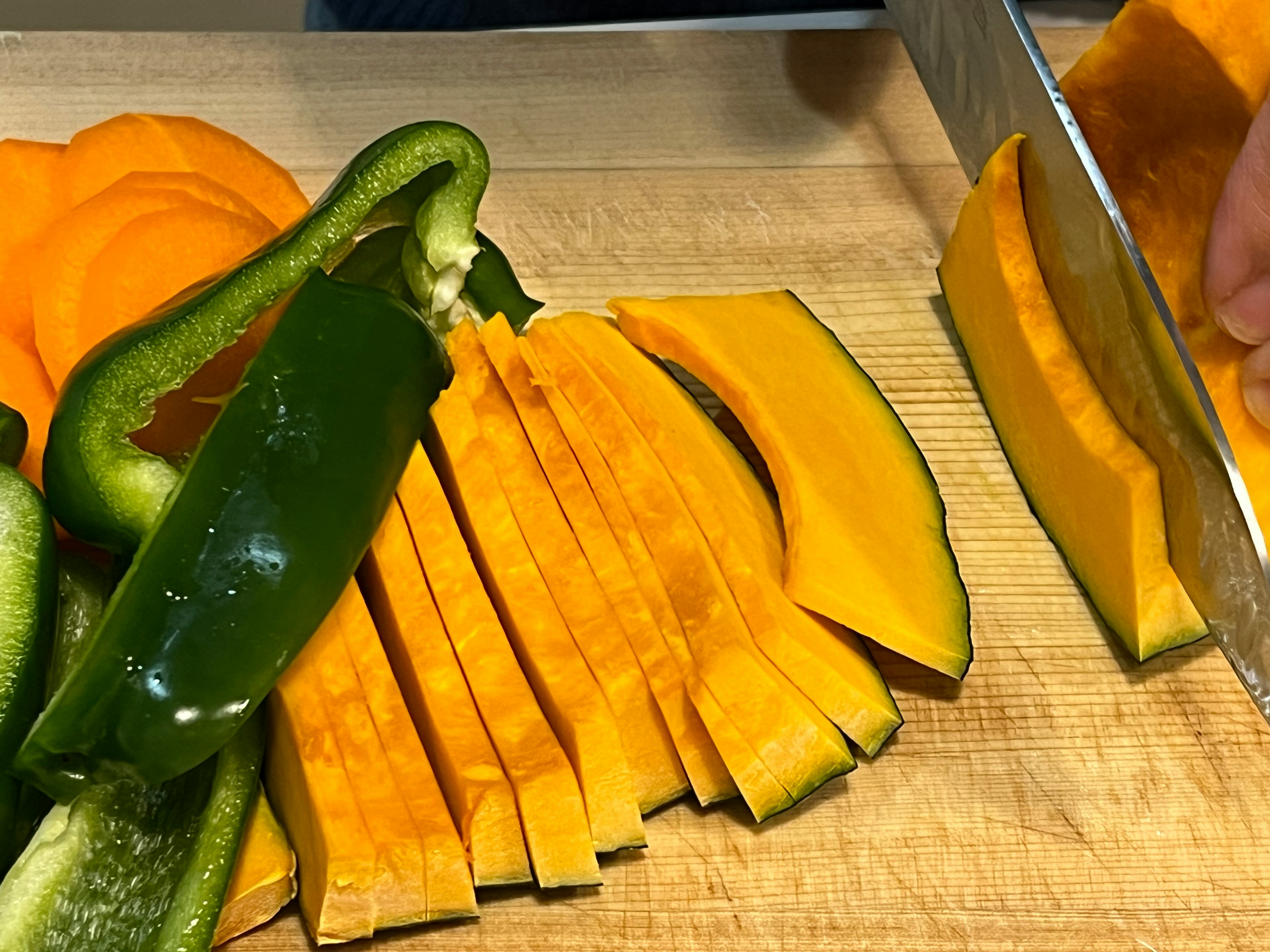 Gambar menunjukkan labu dan paprika yang diiris di atas papan pemotong kayu