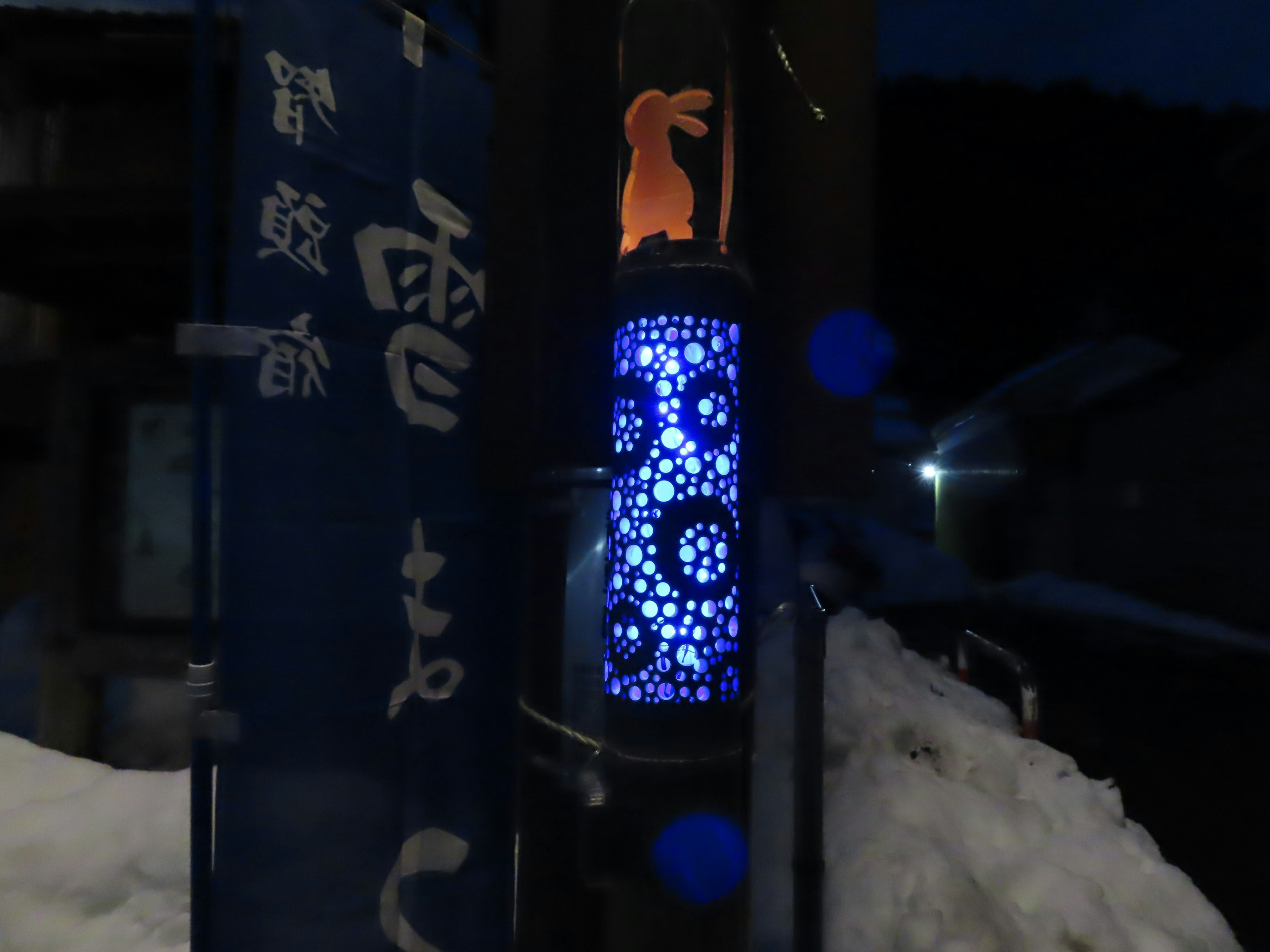 Lámpara azul iluminada con patrones florales y una silueta de conejo en la nieve