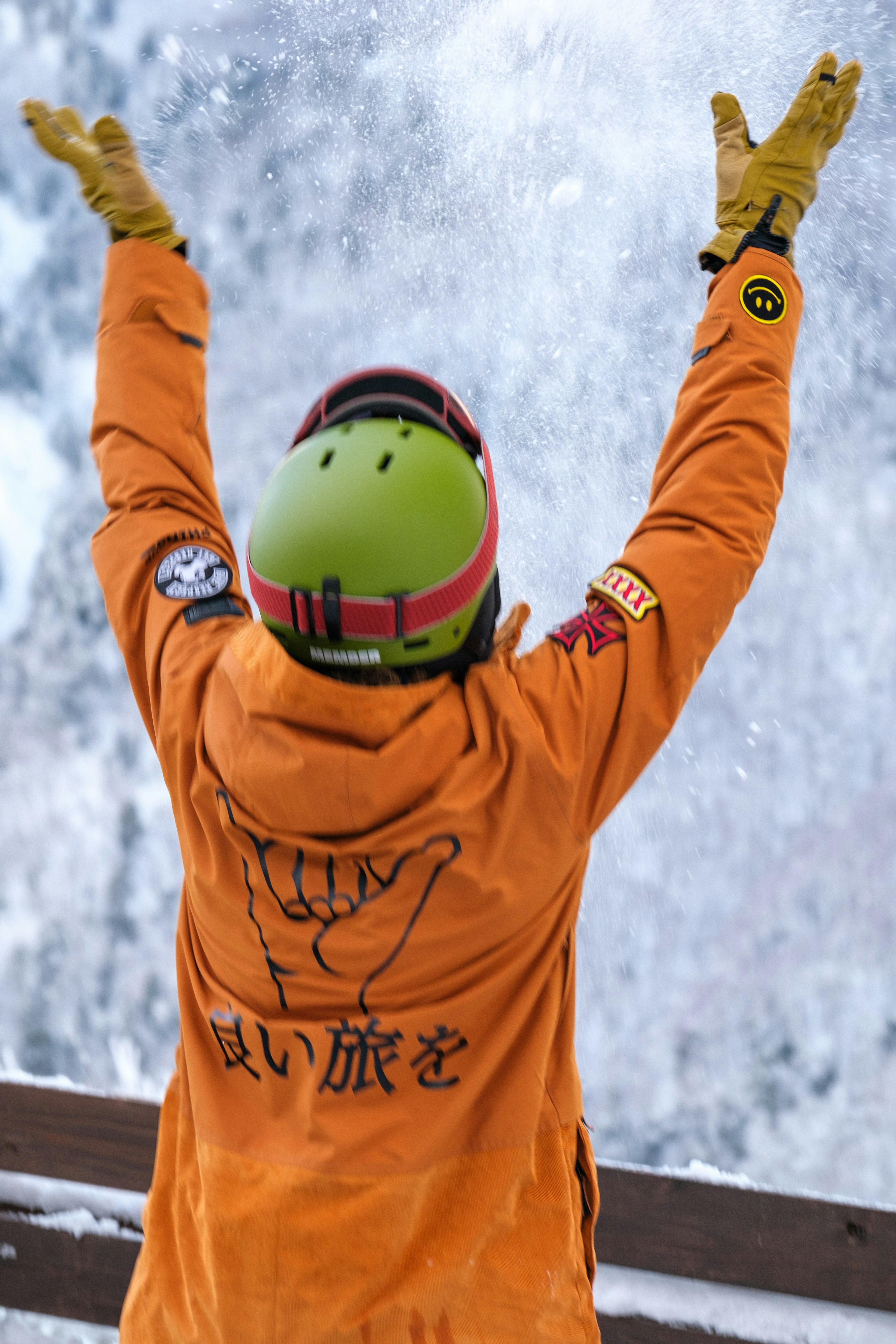 Person, die Freude auf einer Skipiste ausdrückt, trägt eine orange Jacke und einen grünen Helm