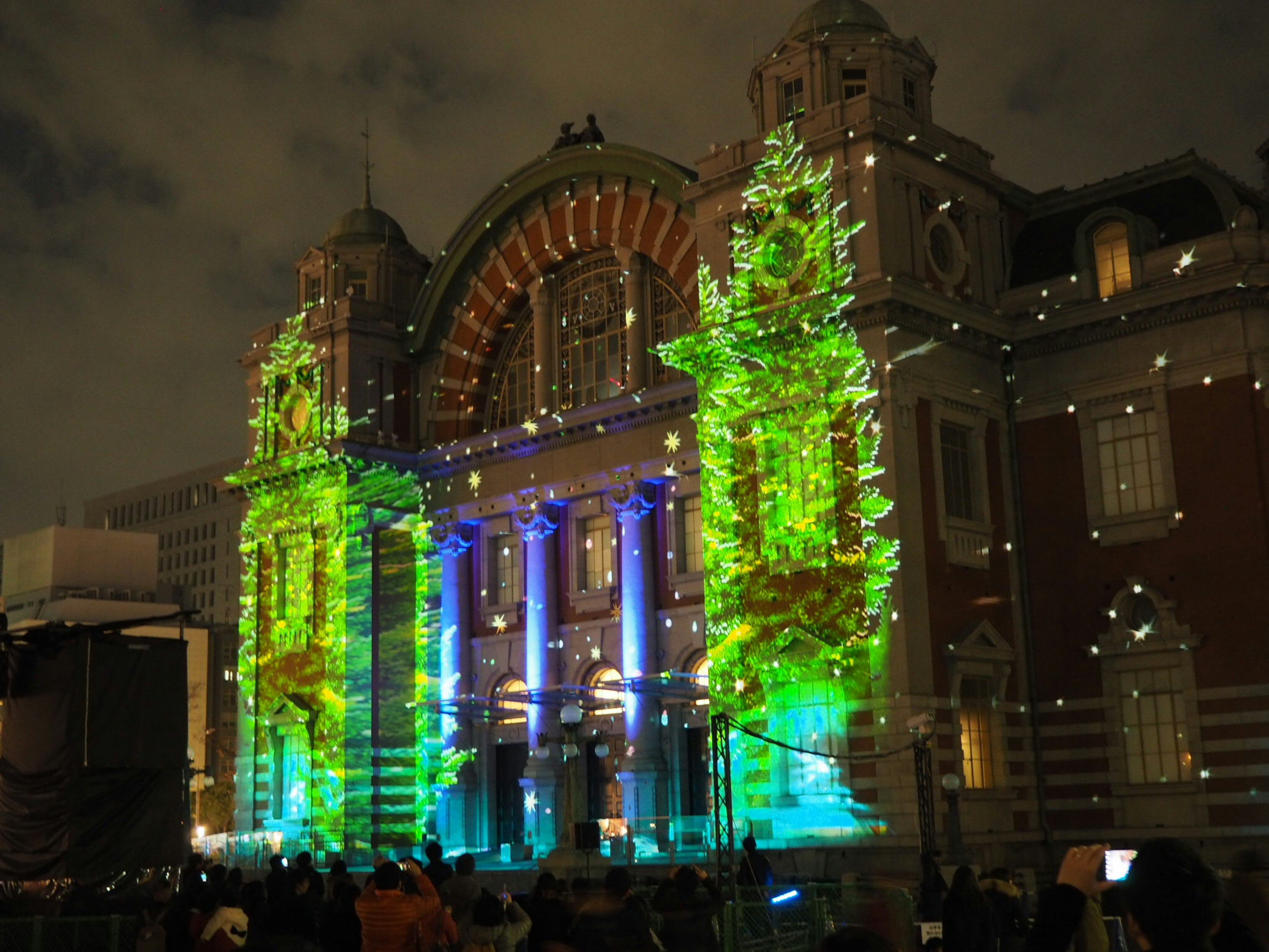 Fachada de un edificio histórico iluminada de noche con luces coloridas personas reunidas