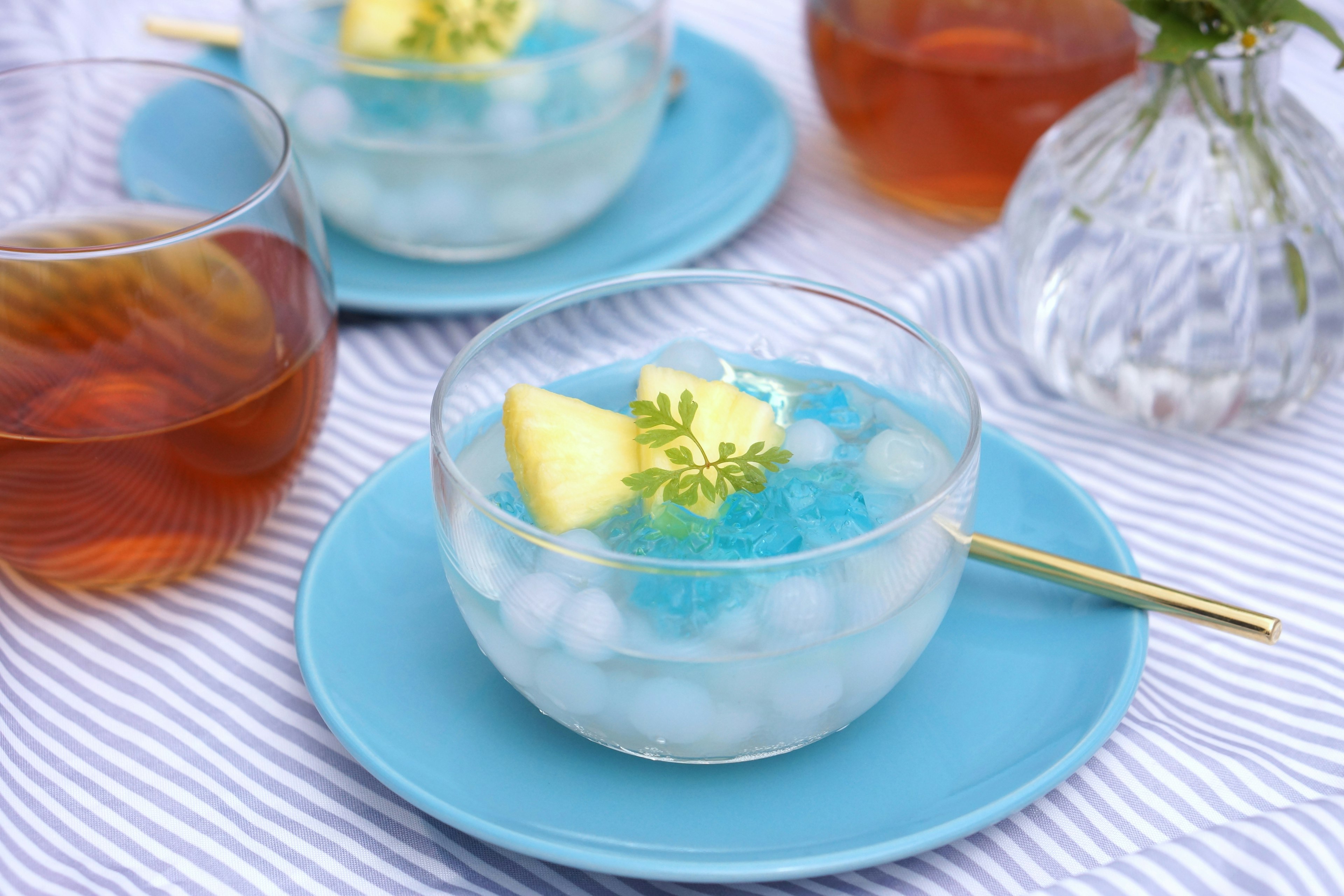 Gambar makanan penutup dalam mangkuk bening dengan jeli biru dan es yang dihiasi dengan irisan nanas dan daun