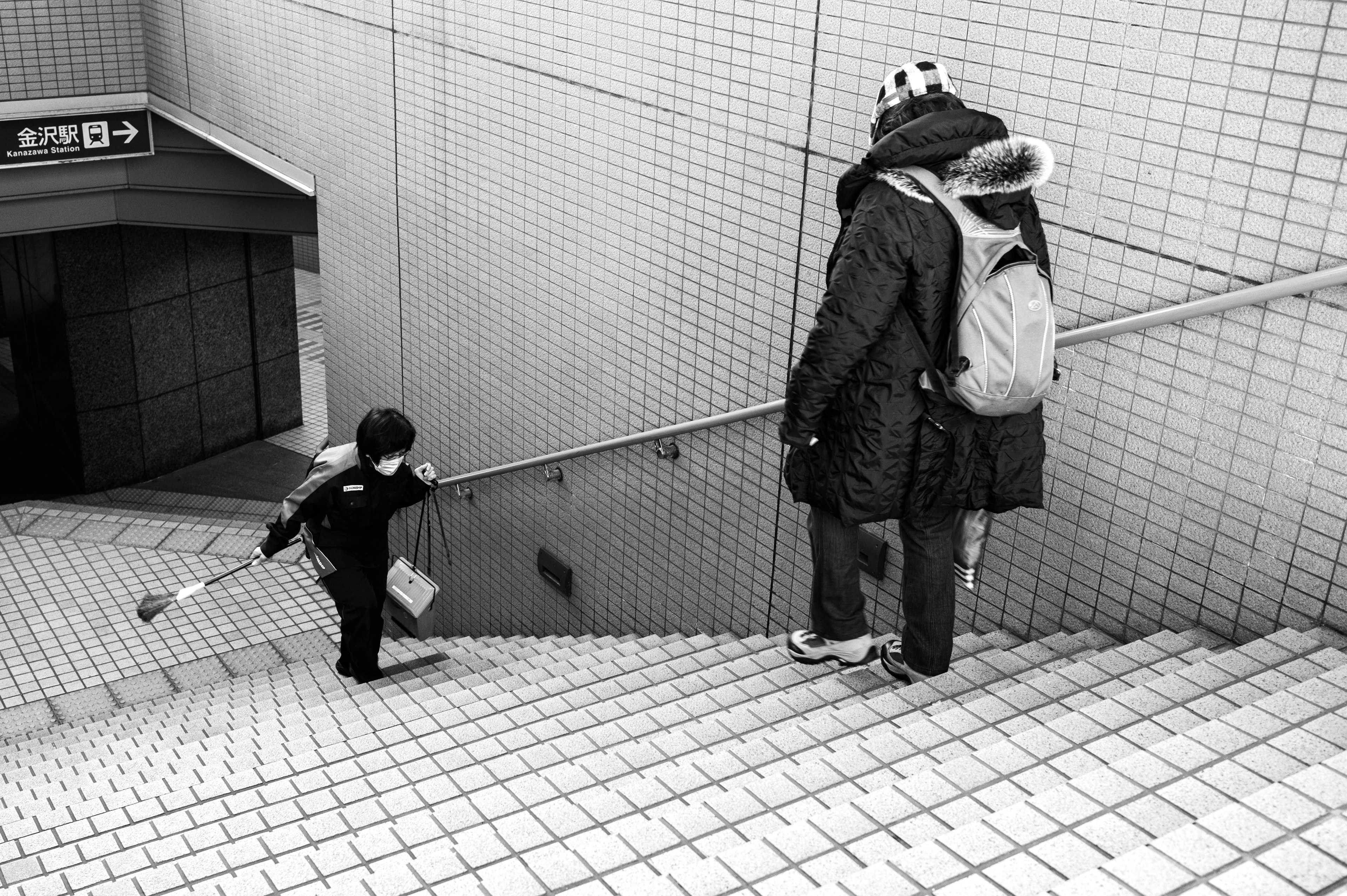 Child descending stairs while an adult stands nearby in black and white