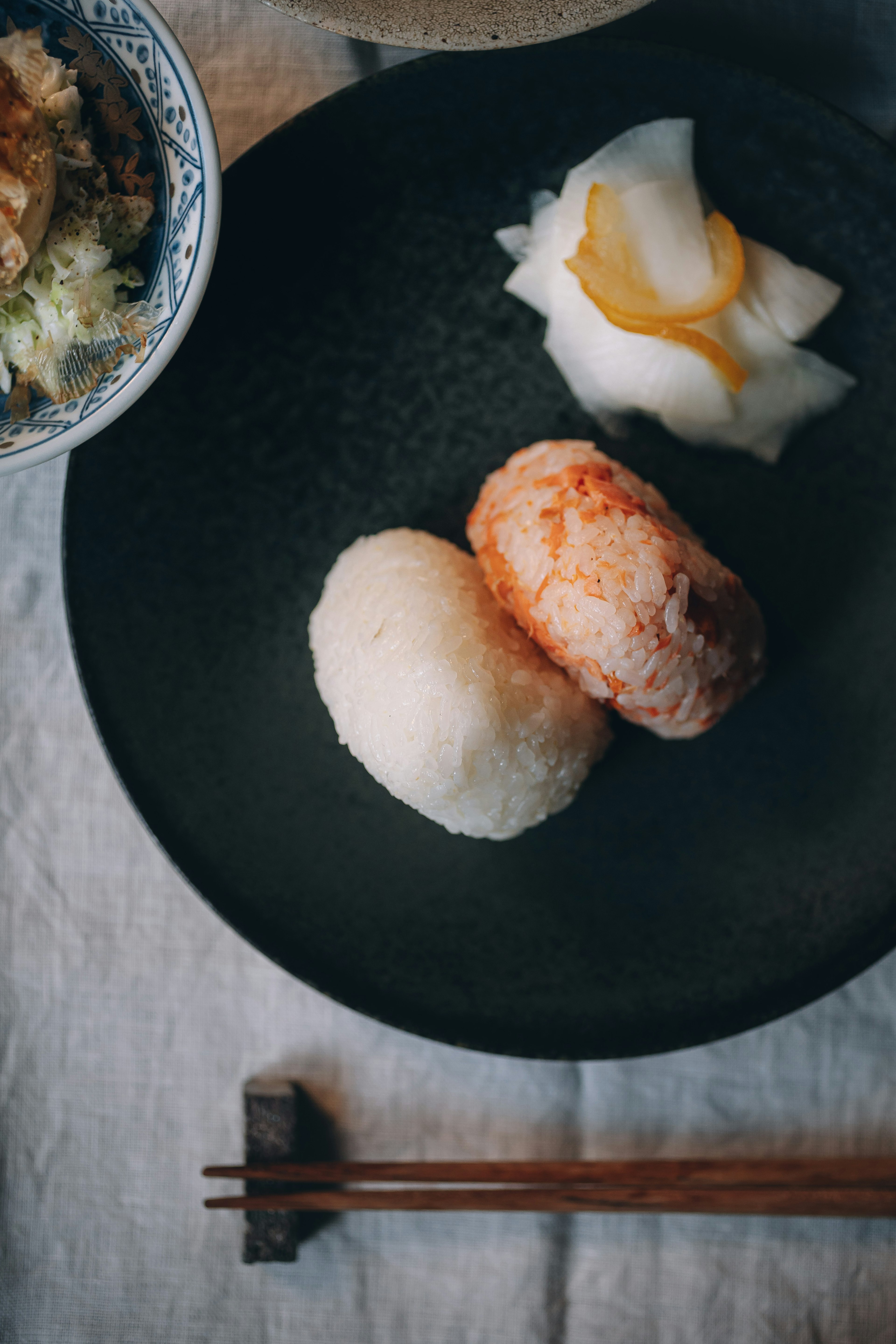 Two different rice balls on a black plate with pickled vegetables