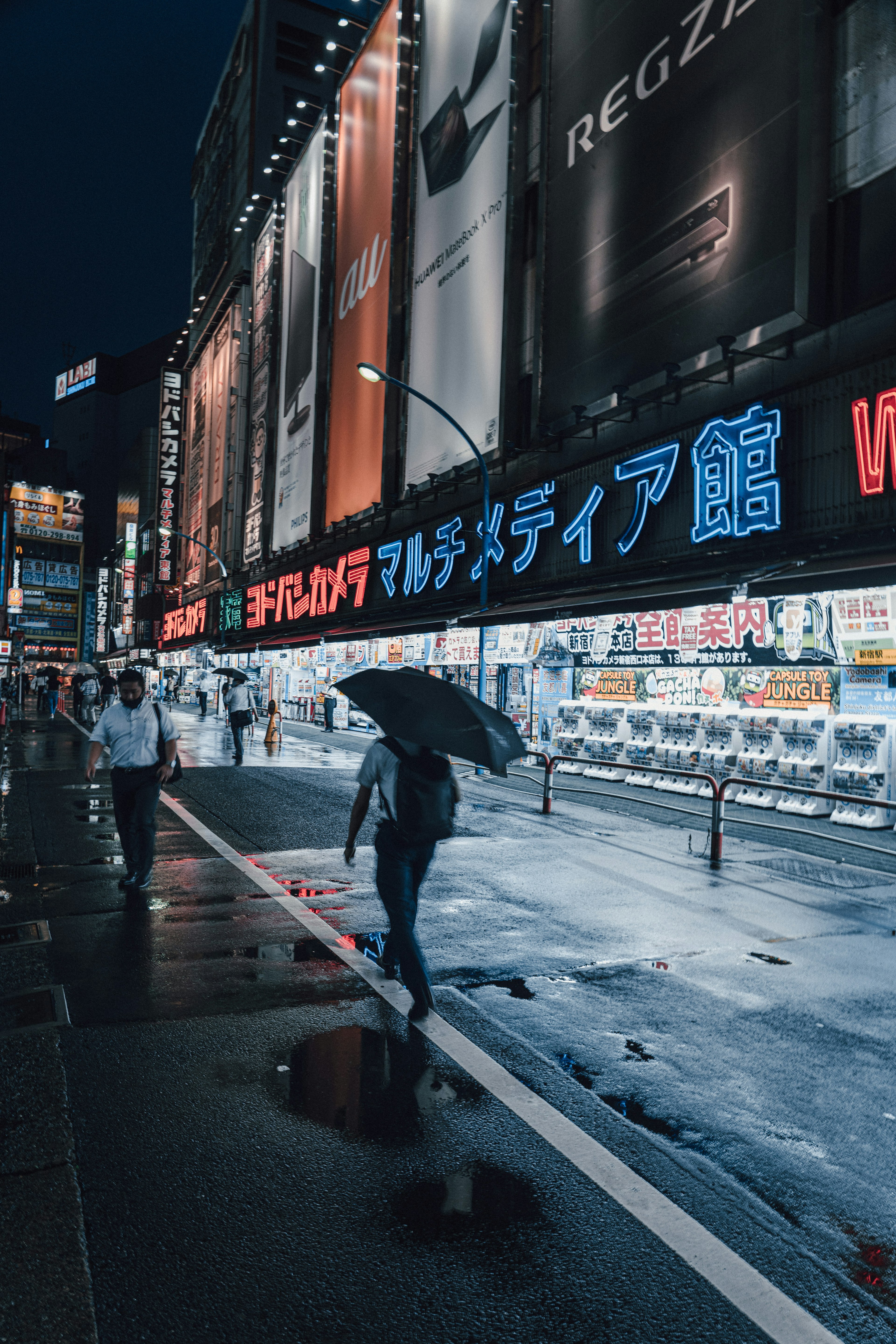 A person walking with an umbrella on a rain-soaked street at night