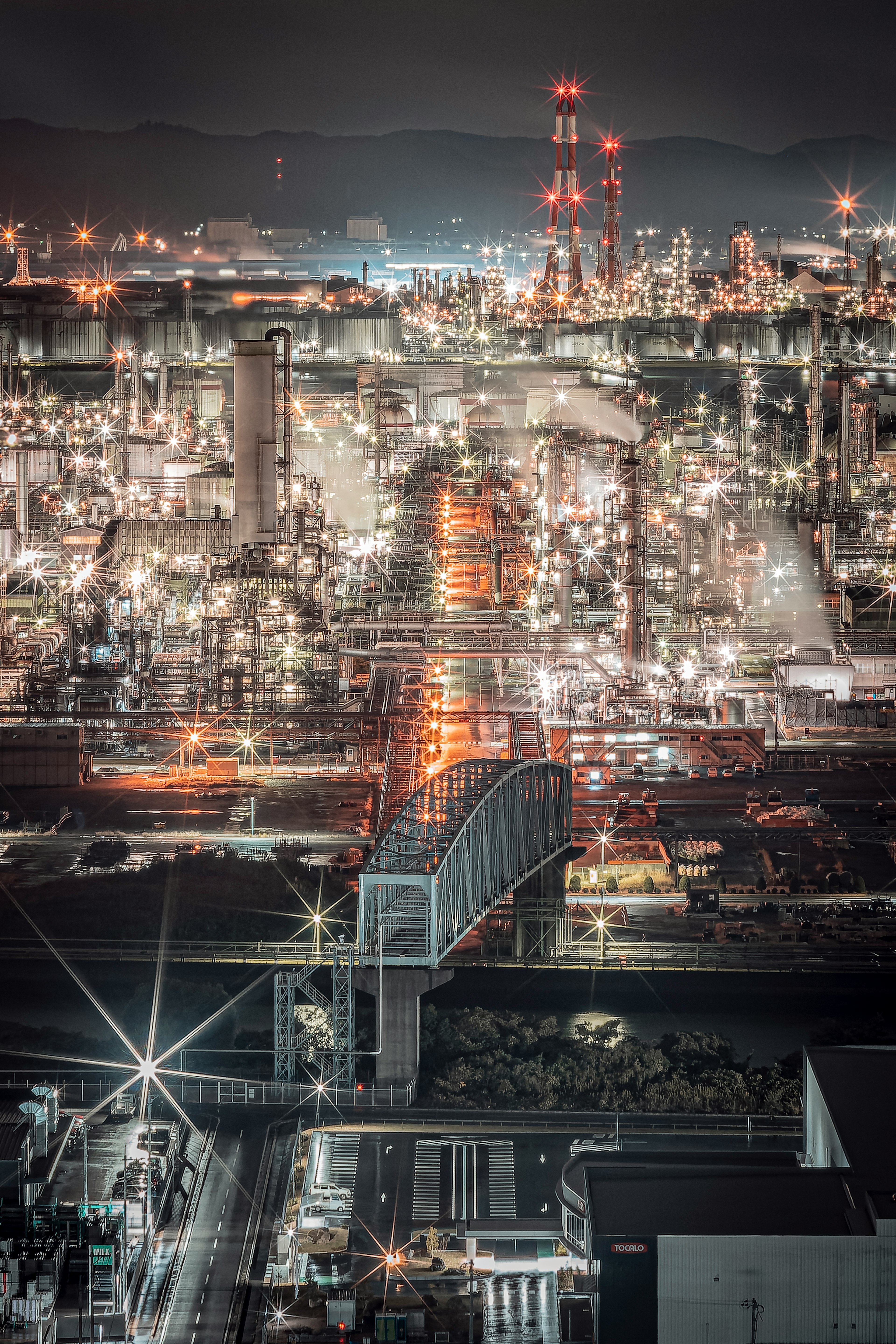 Vibrant industrial landscape at night with bright factory lights and a bridge