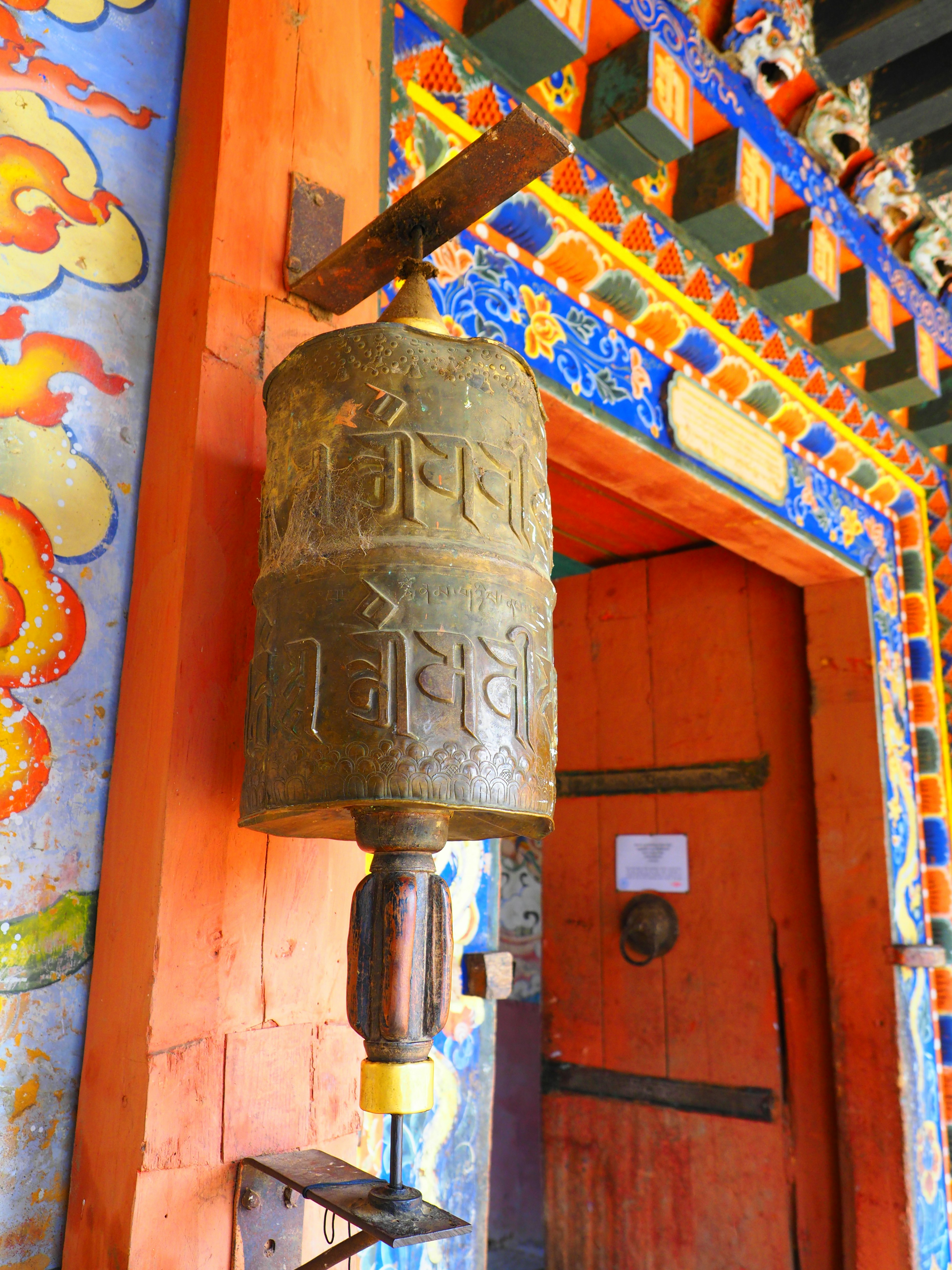 Bronze prayer wheel hanging at a temple entrance with vibrant decorations